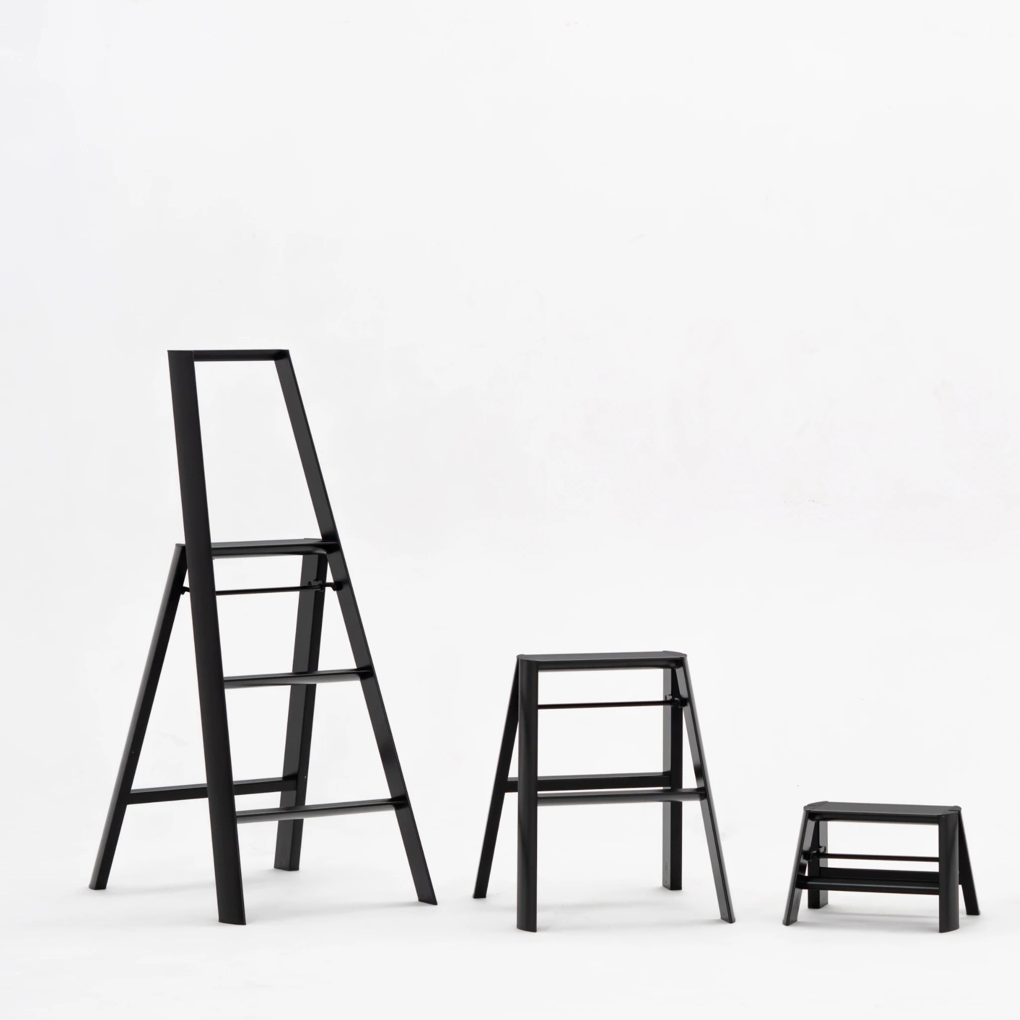 Drie Hasegawa zwart trapkrukken-Lucano Ladder 3 Trede, een hogere viertrede en een kleine tweetrede- worden weergegeven op een witte achtergrond, waardoor hun slanke zwarte ontwerp wordt benadrukt.