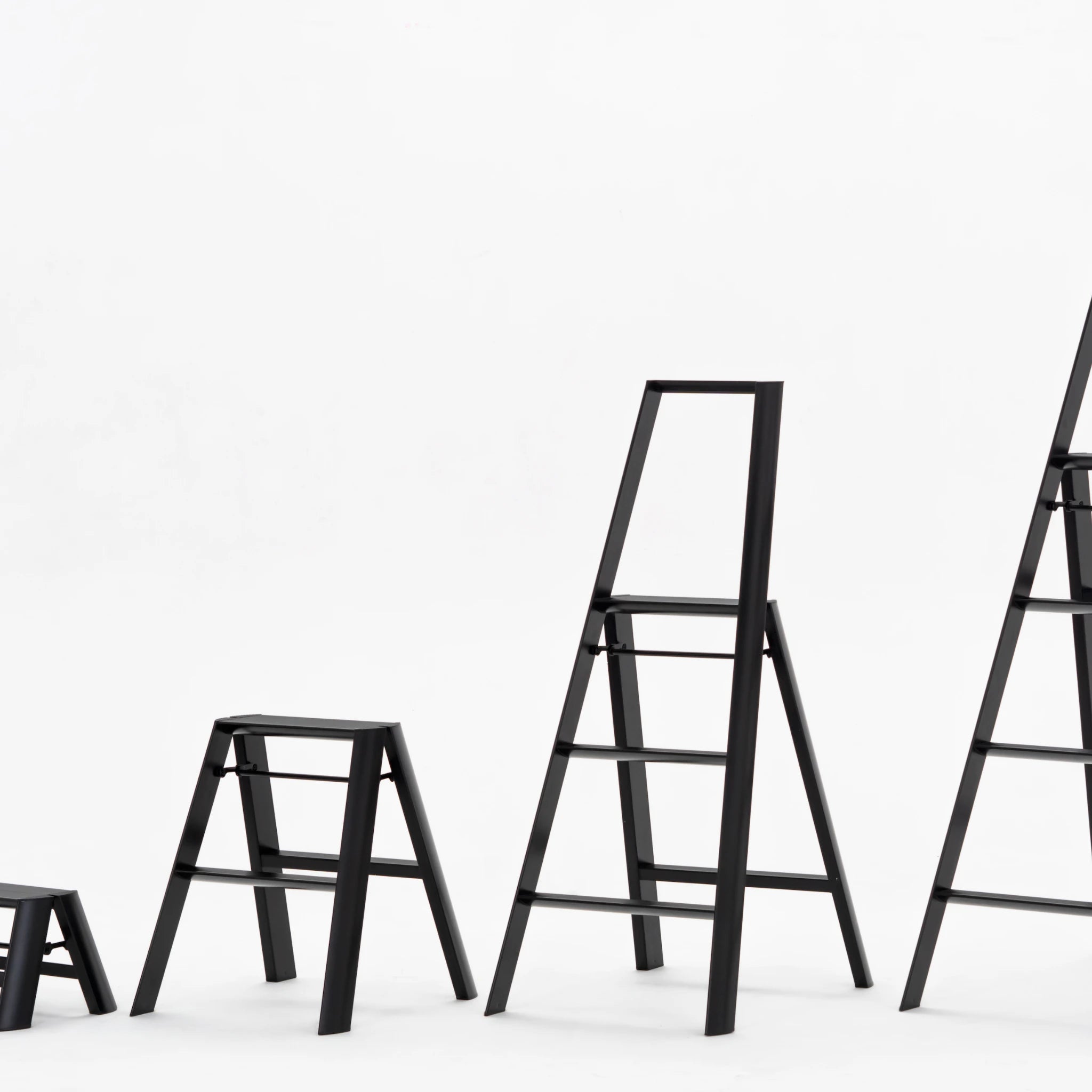 Vier Hasegawa Lucano Ladder 3 Stappen Zwart trapladders van Hasegawa, geïnspireerd op Japans design, staan in een rij op een effen witte achtergrond en tonen een progressie van de kortste naar de langste.