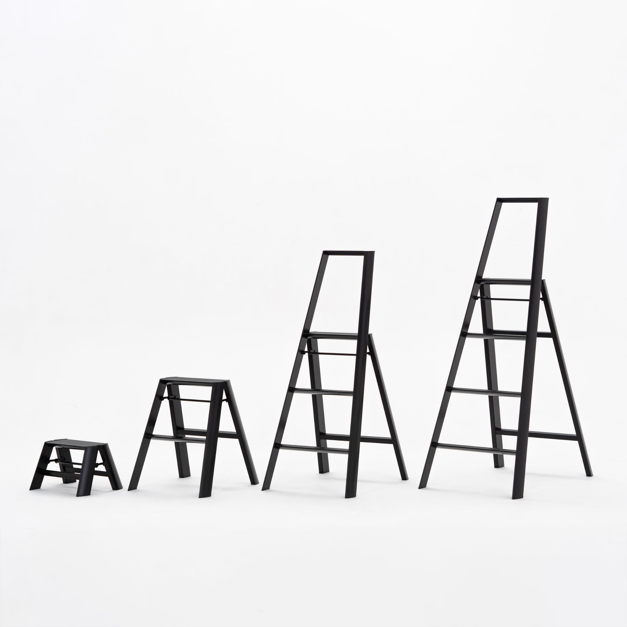 Vier Hasegawa Lucano Ladder 4 Stappen Zwart ladders, elk hoger dan de vorige, zijn opgesteld van links naar rechts tegen een effen witte achtergrond, die hun minimalistische, moderne ontwerp laat zien.