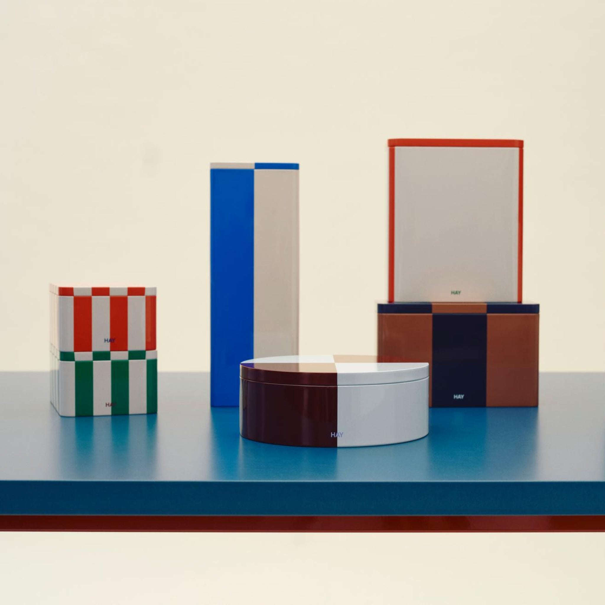 De Hay Blikken Doos Blauw Off-White Slim van Hay staat op een blauw oppervlak tegen een neutrale achtergrond en toont modern Scandinavisch design met gedurfde blauwe en gebroken witte kleuraccenten.