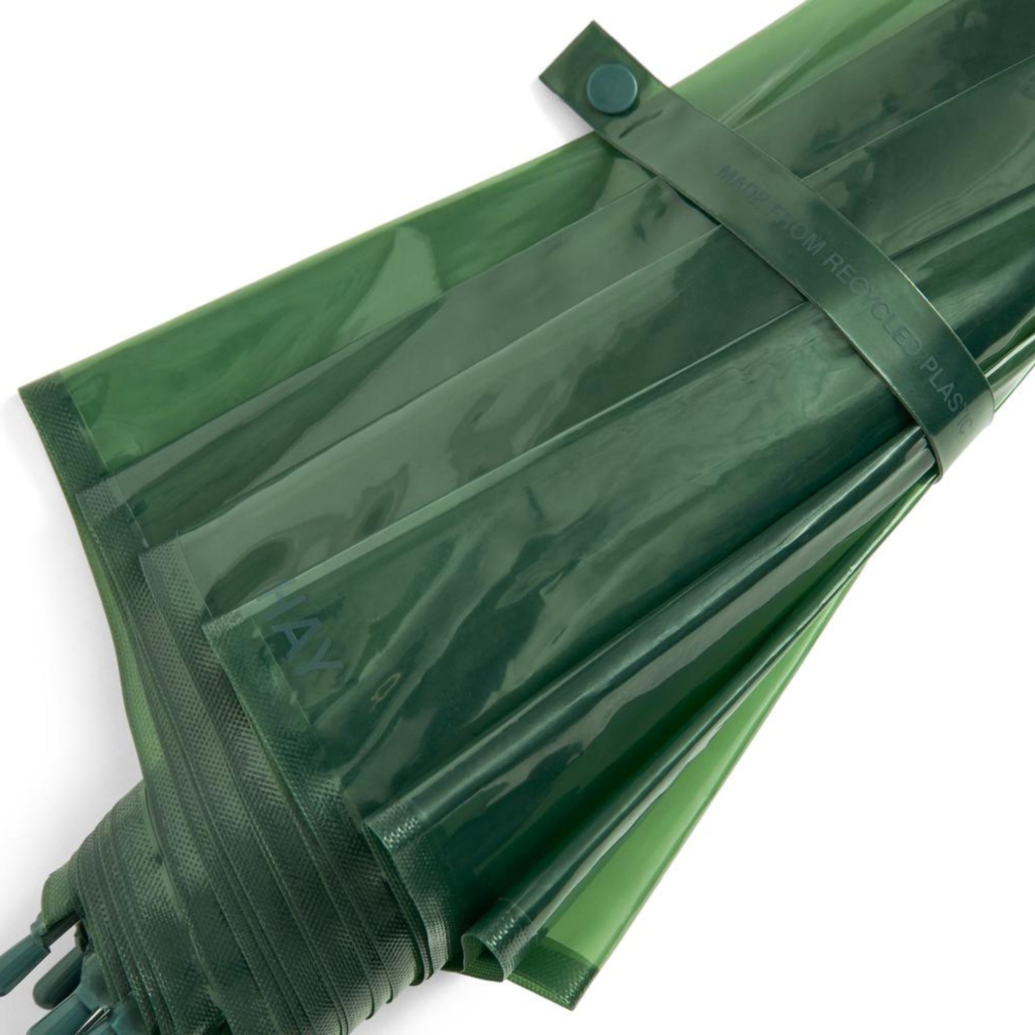 Close-up van de Hay Canopy Paraplu Groen van Hay, gevouwen en vastgezet met een bijpassende riem en drukknoop. Deze duurzame paraplu is gemaakt van gerecycled materiaal en heeft een waterafstotend scherm met een subtiele glanzende afwerking.