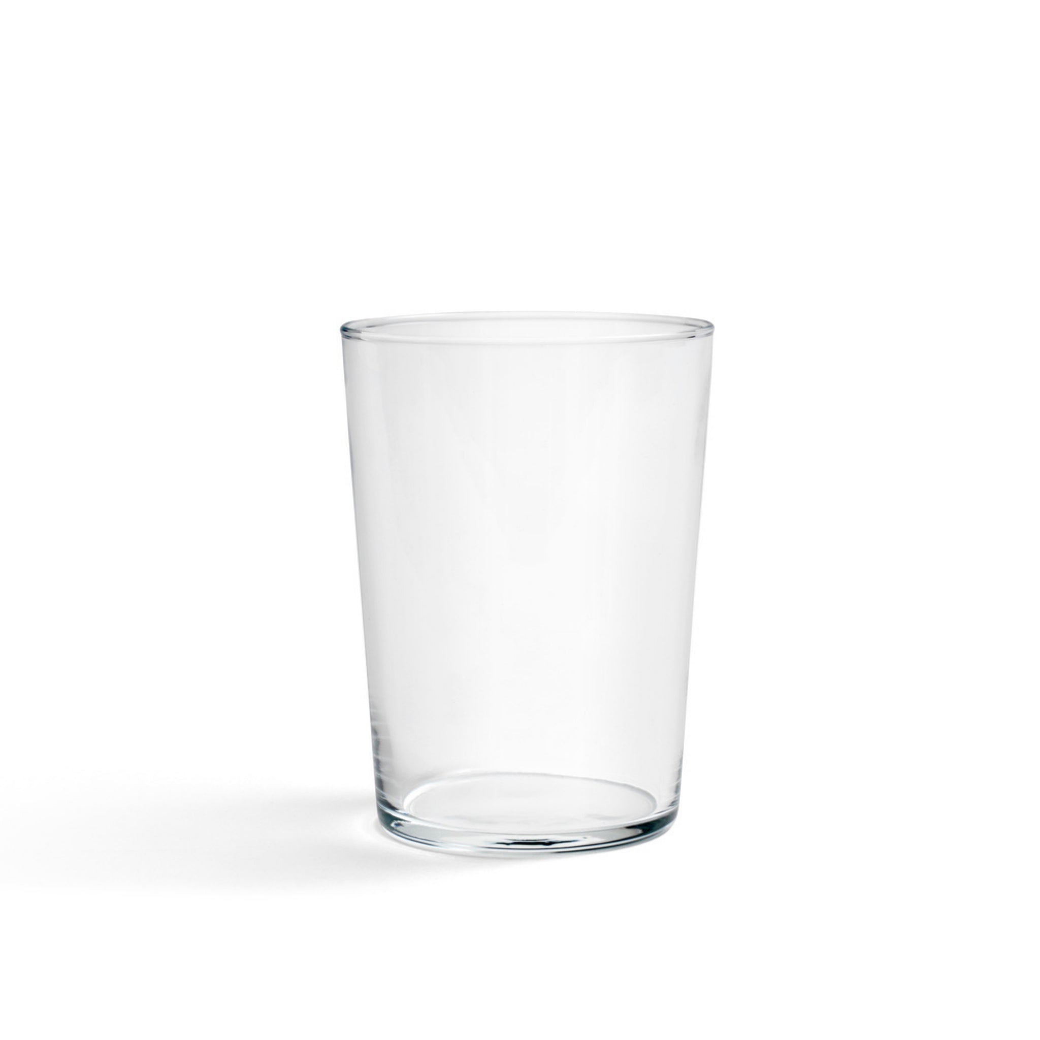 Een heldere Glas Helder L beker van Hay staat in het midden op een witte achtergrond, met een vage schaduw aan de linkerkant - een perfect voorbeeld van minimalistisch glazen.