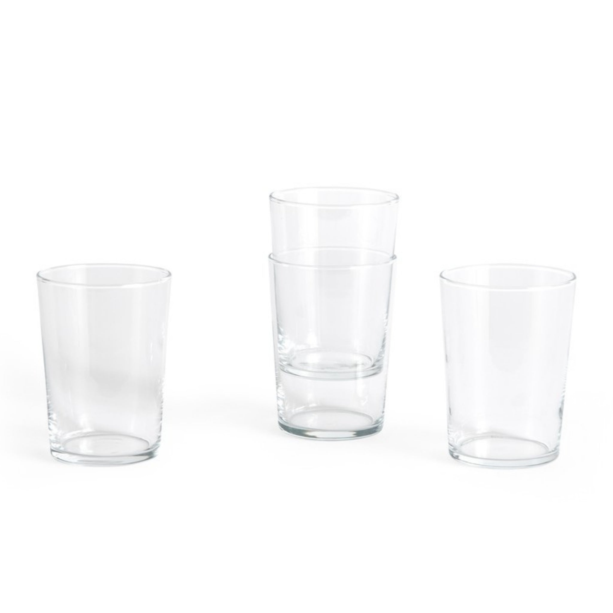 Vier heldere Hay Glas Helder L tumblers van Hay staan op een witte achtergrond. Twee glazen zijn gestapeld en de andere twee staan los van elkaar, waardoor hun minimalistische ontwerp en stapelbare vorm goed tot zijn recht komt.