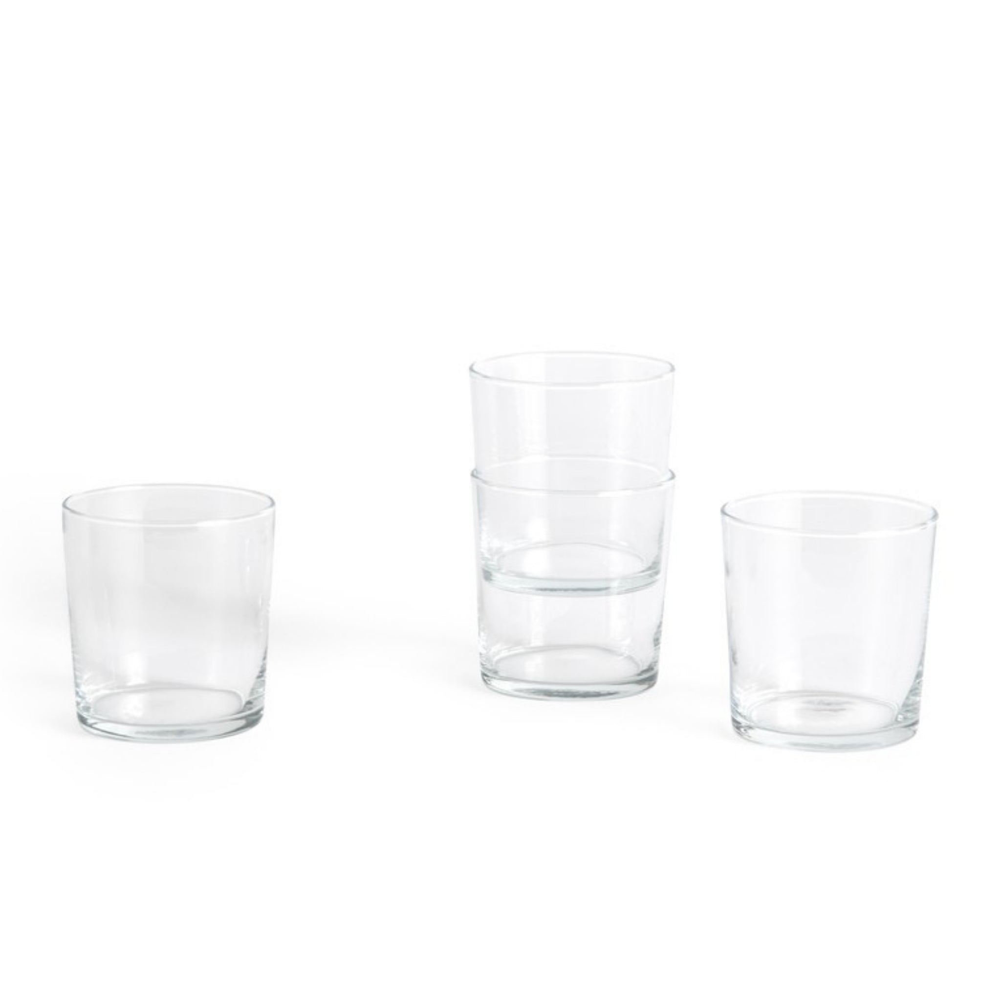 Vier heldere, minimalistische Hay Glas Helder M tumblers van het merk Hay staan op een witte ondergrond. Drie glazen zijn gestapeld en gegroepeerd, terwijl het vierde glas links apart staat.