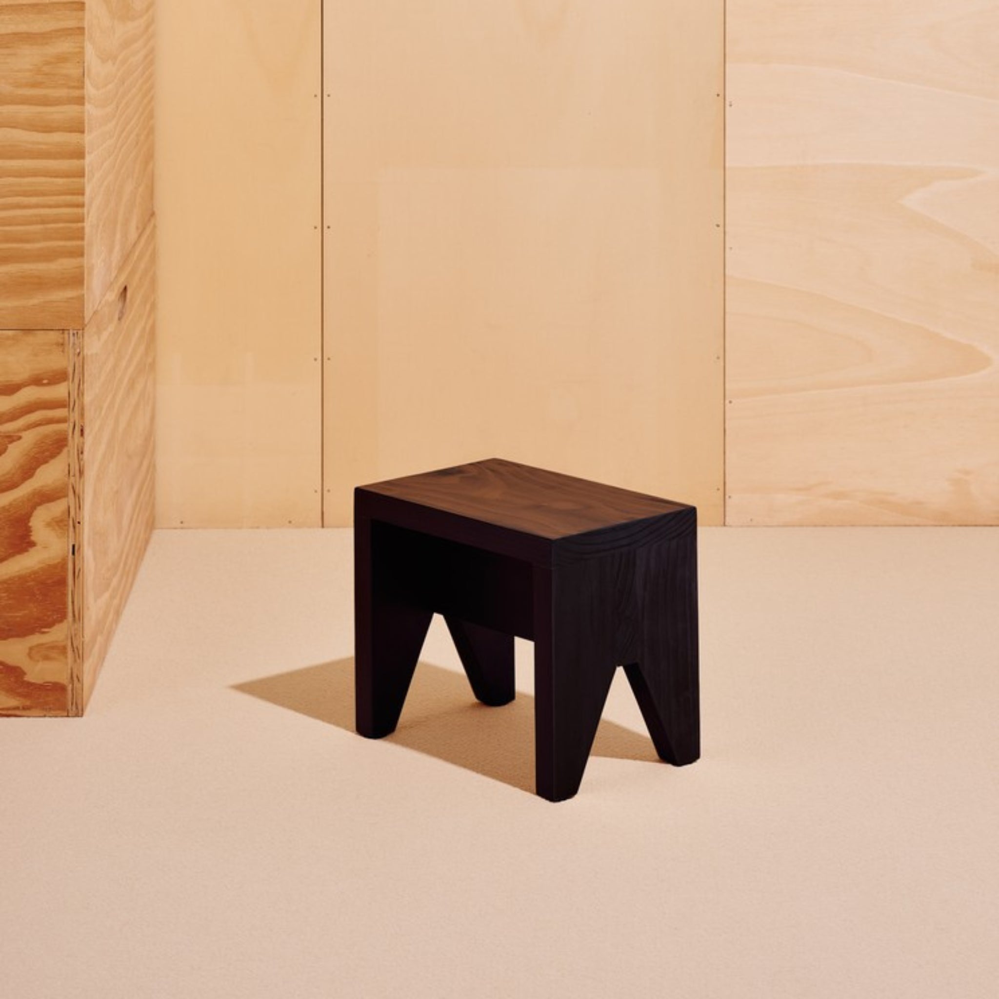 De Hay Manolito Kruk Zwart Kort van Hay, een compacte donkere kruk met schuine poten, staat op een lichtbeige vloer tegen wanden met houten panelen - een ideale zwarte kruk voor moderne interieurs.