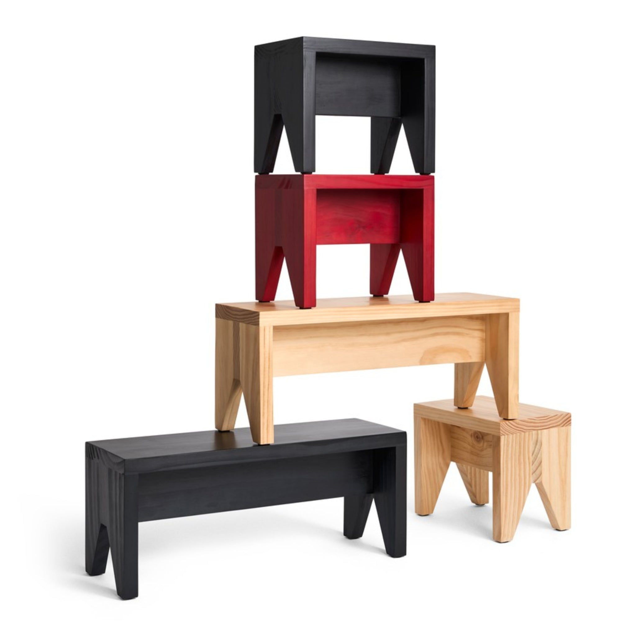 Vier houten banken en Hay Manolito Stool Bank Naturel Lang krukjes van Hay in zwart, rood en natureltinten zijn speels gestapeld, waardoor een compacte piramide is ontstaan met banken boven elkaar.