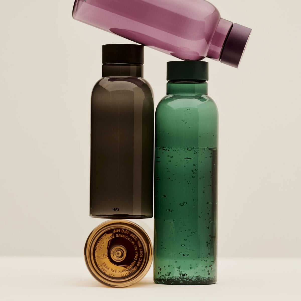 De Hay Miz Waterfles Donkergroen 720 ml staat naast een charcoal Miz fles, met een paarse fles er dwars bovenop en een dop op de voorgrond.