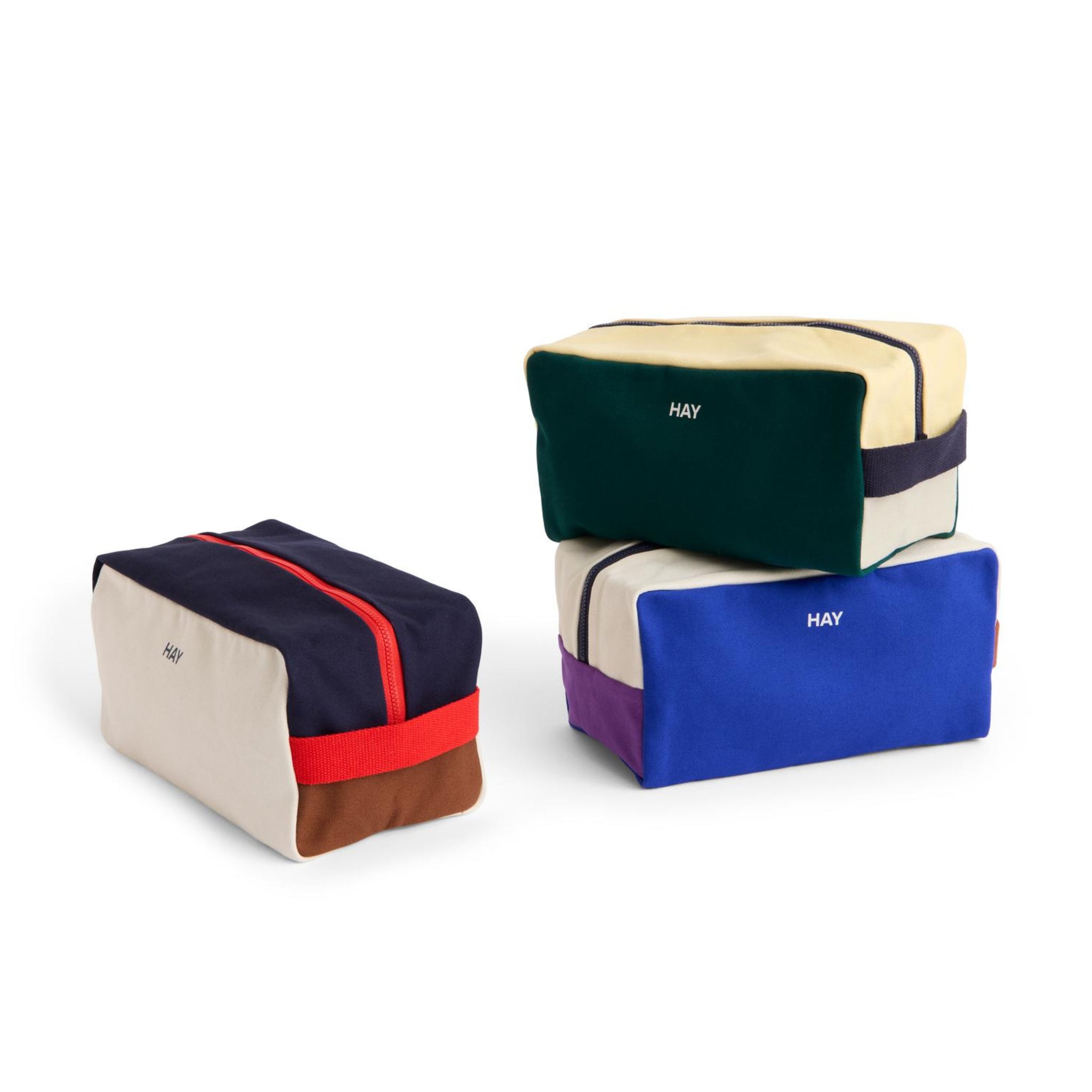 Drie rechthoekige Hay Multi Toilettas Medium Crème tassen, elk met een zichtbare rits en HAY logo, worden getoond: twee gestapeld, één ernaast.
