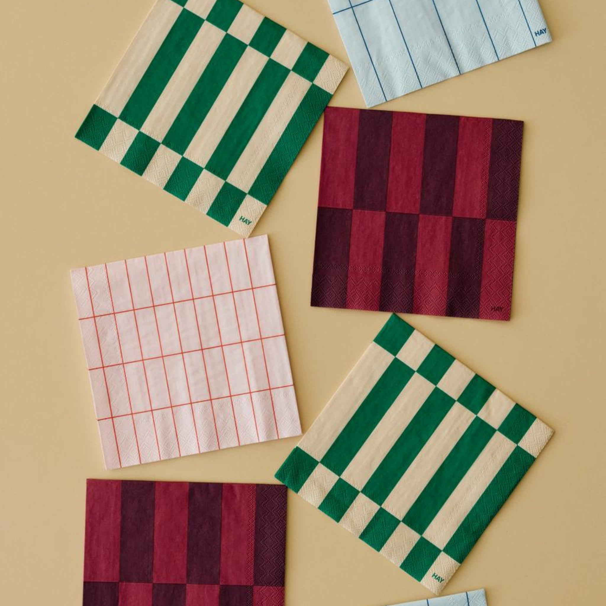 Hay Pattern Papieren Servetten Lichtroze Rood Grid 40/40 van Hay, met unieke rasterontwerpen in levendig rood op lichtroze, zijn gerangschikt op een beige oppervlak. Elke servet heeft een duidelijke lijndikte voor een stijlvolle touch.