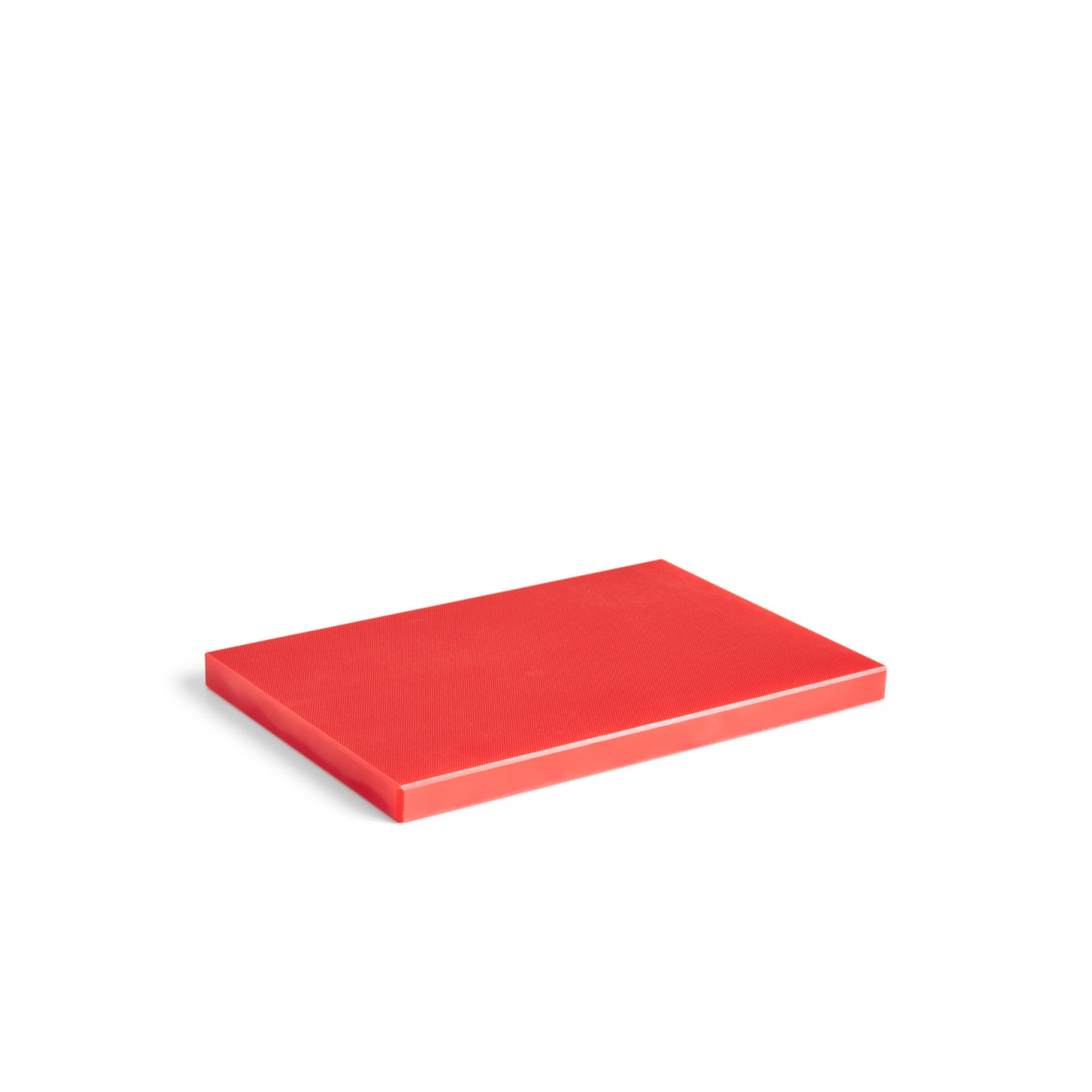 Een gesloten, rechthoekig rood boek of notitieblok ligt plat op een wit oppervlak en lijkt qua vorm en kleur op de Hay Slice Snijplank Rood 20/30 van Hay.