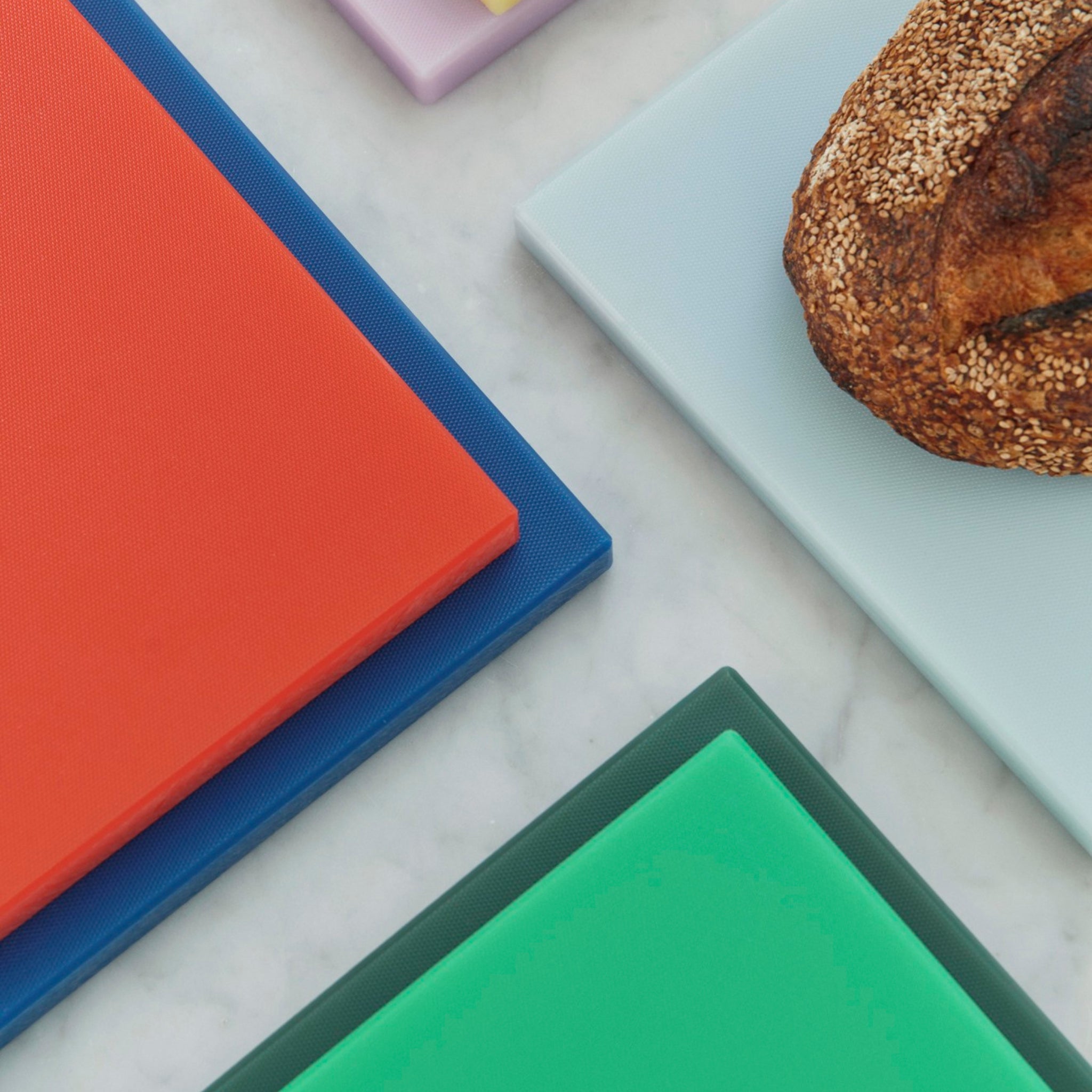 De Hay Slice Snijplank Donkerblauw 25/38 van Hay staat op een marmeren keukenblad, met een brood met zaadjes op de stijlvolle donkerblauwe snijplank.