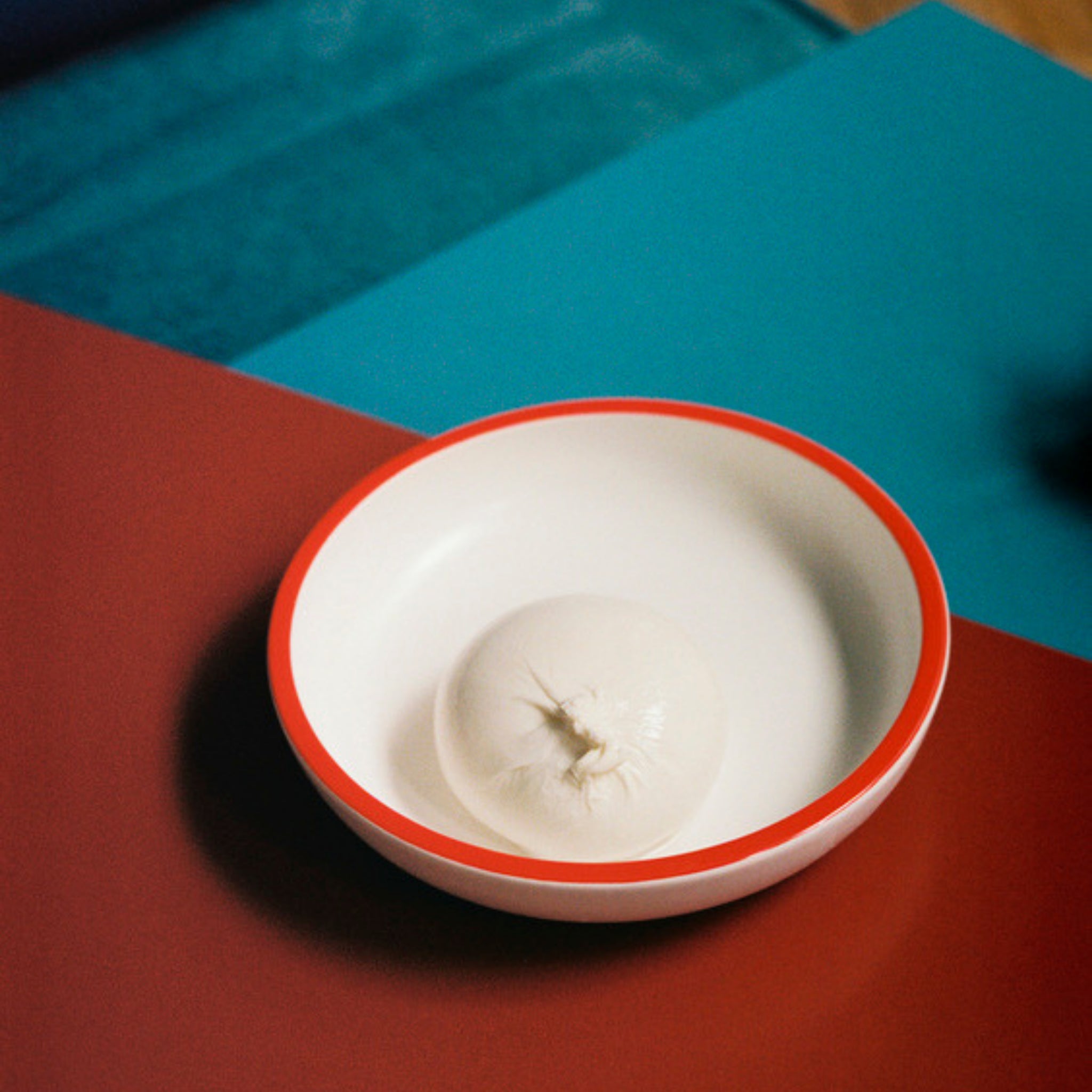 Een wit bolletje burrata kaas wordt geserveerd in een wit porseleinen schaaltje met een rode rand, geplaatst op de Hay Sobremesa Serveerschaal Wit, Rode Rand D20 van Hay.