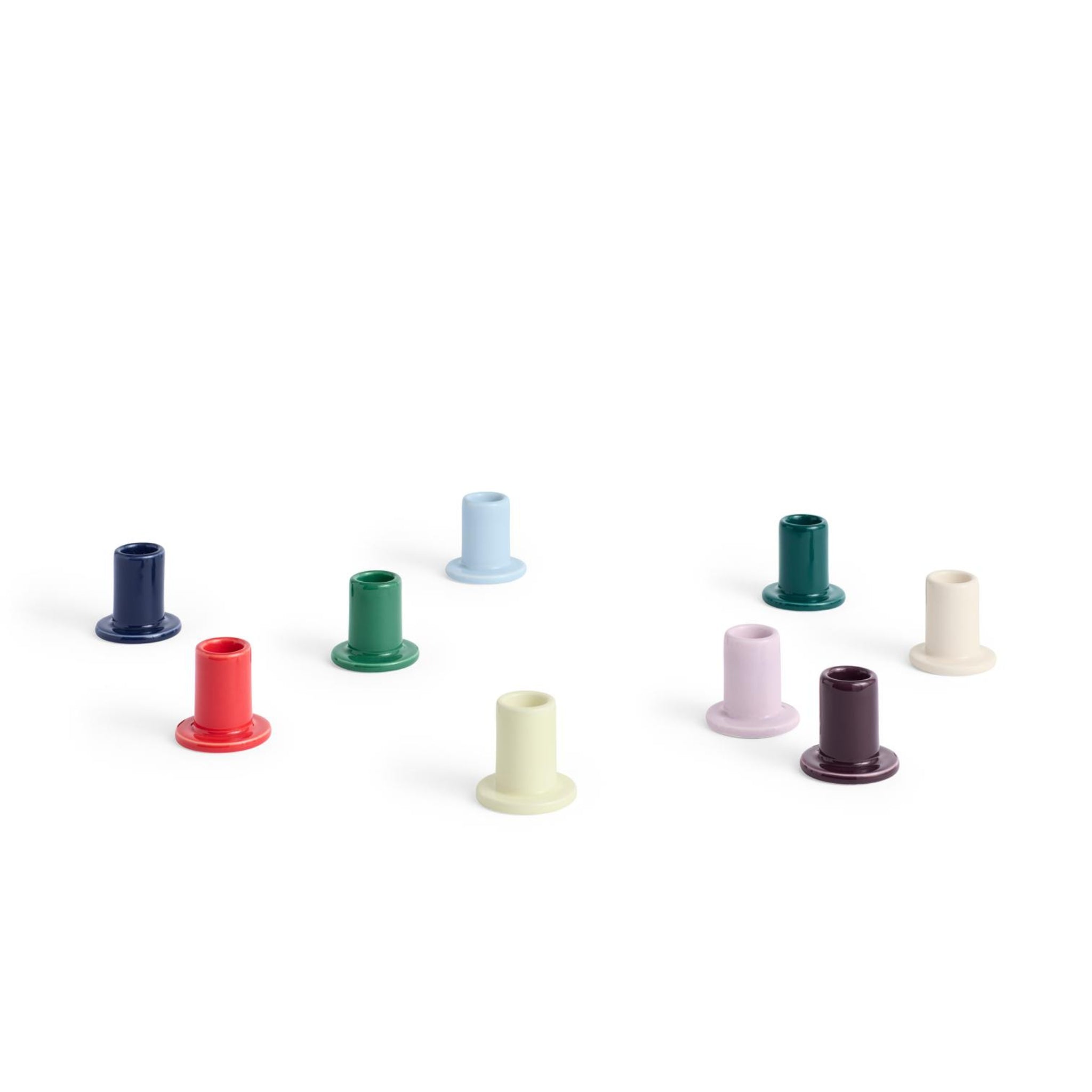 Acht kleine Hay Tube Kandelaar kandelaars van Hay, elk met een uitlopende voet, worden weergegeven op een witte achtergrond in rood, blauw, groen, crème, lichtgeel, paars en bordeaux.