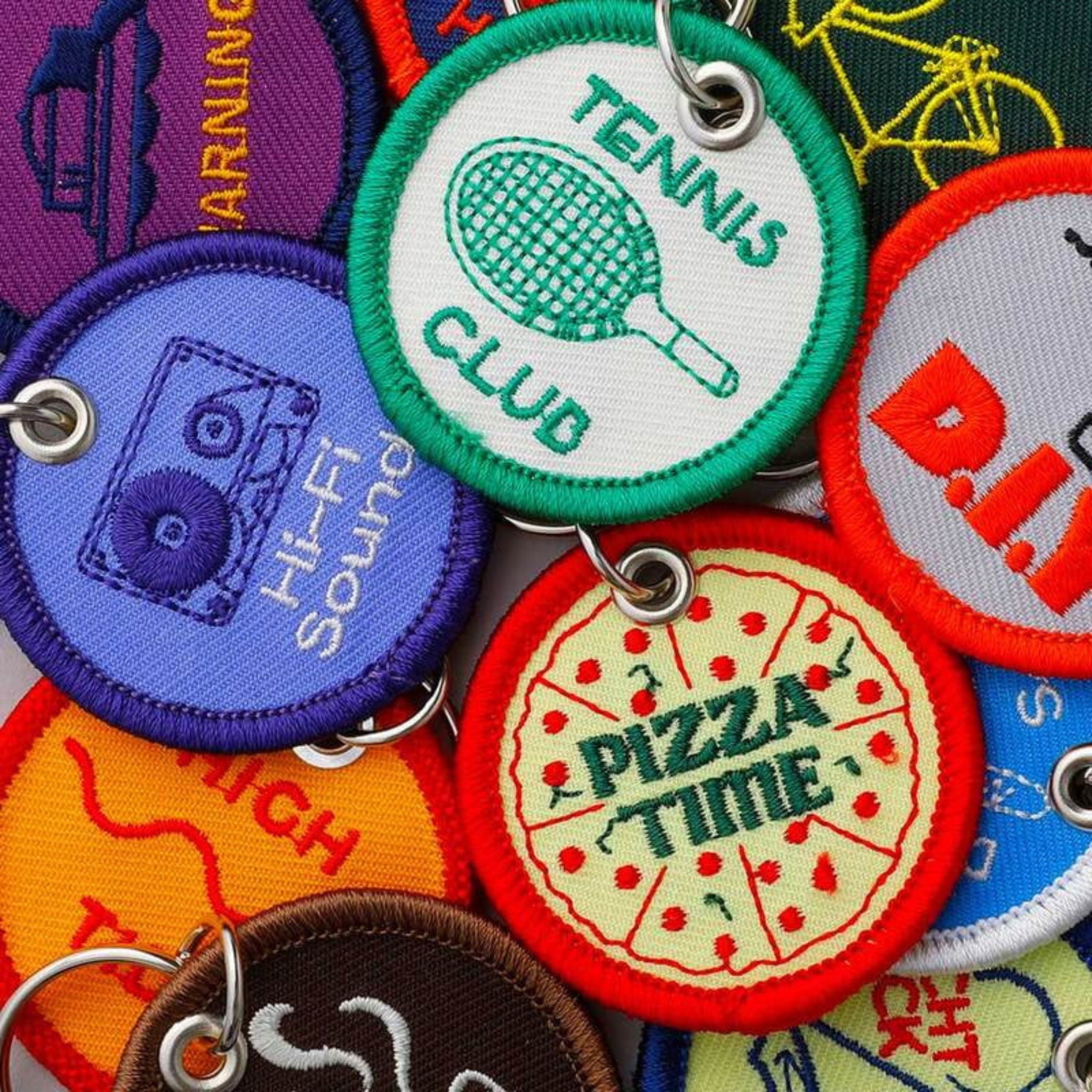 Een close-up van speelse Hightide Stitch Work Sleutelhanger Pizza sleutelhangers, met kleurrijke geborduurde ontwerpen zoals "PIZZA TIME" met een pizzaplak, van Hightide.