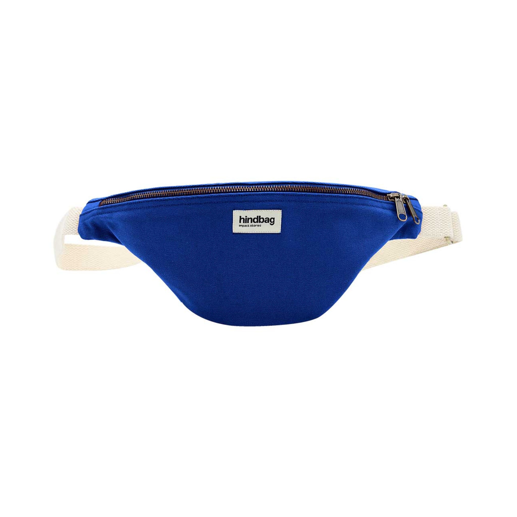 De Hindbag Olivia Heuptasje Elektrisch Blauw is een blauwe heuptas van biologisch katoen, met een beige verstelbare riem, een ritssluiting aan de bovenkant en een klein rechthoekig "hindbag" label op de voorkant.