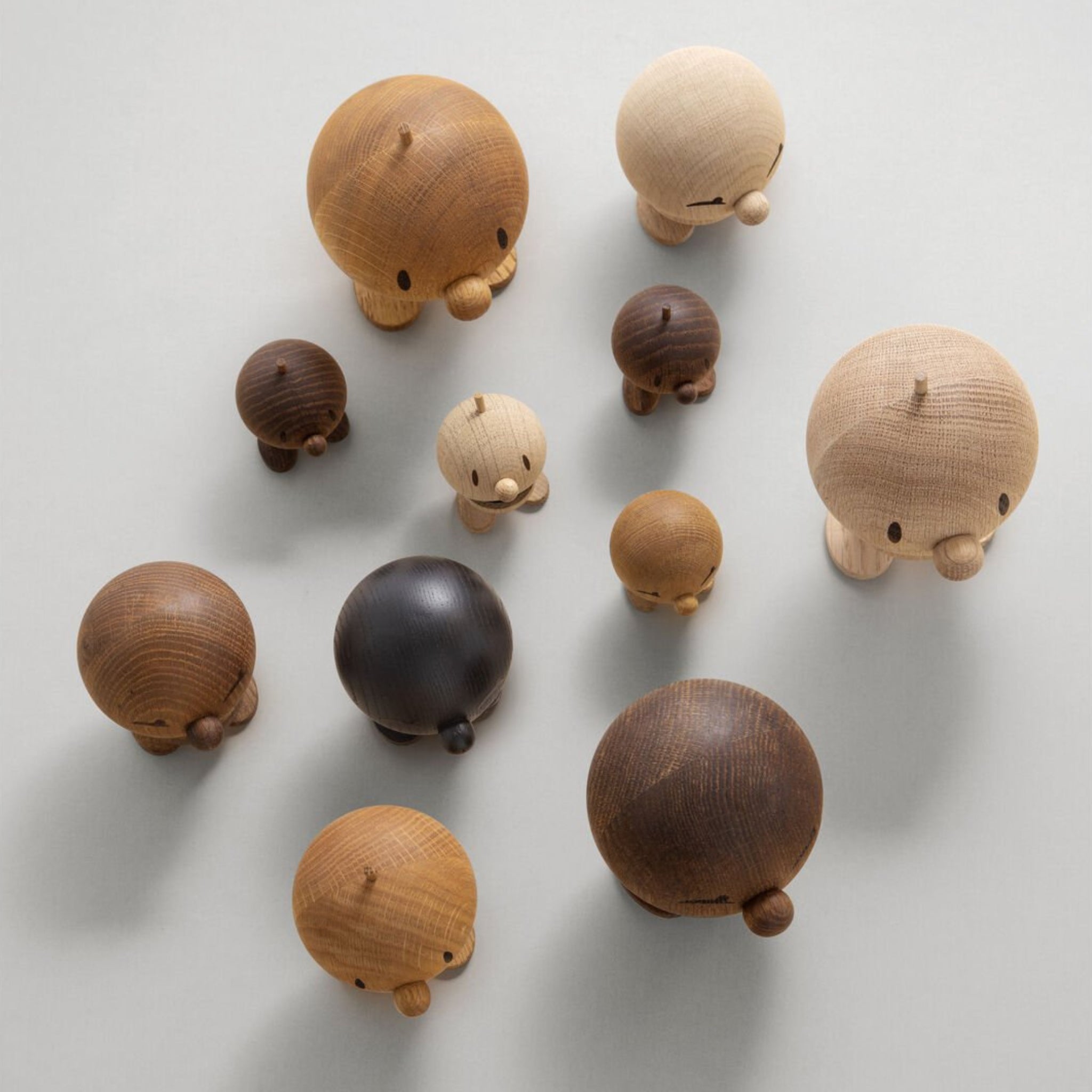 Een verzameling Hoptimist Hout Bumble S Eik van Hoptimist-ronde, houten figuurtjes met kleine pootjes en neuzen in bruine en beige tinten-zijn gerangschikt op een lichtgrijs oppervlak.