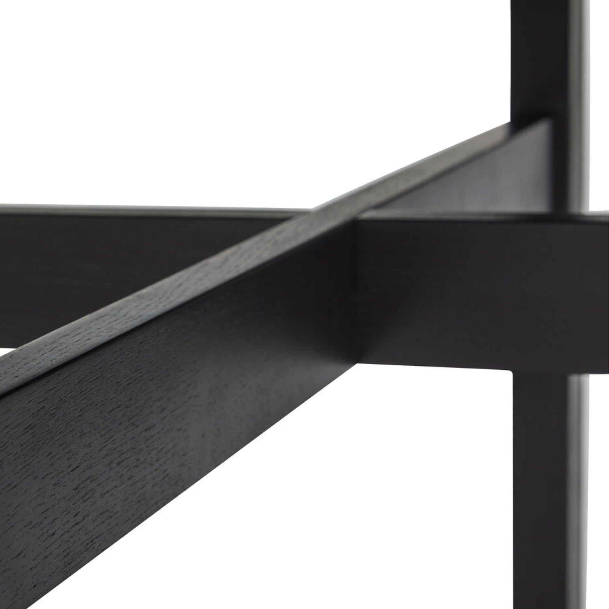 Close-up van kruisende zwarte balken van het Hubsch Fjord Eettafel Essenhout Zwart D120 frame, tegen een witte achtergrond.
