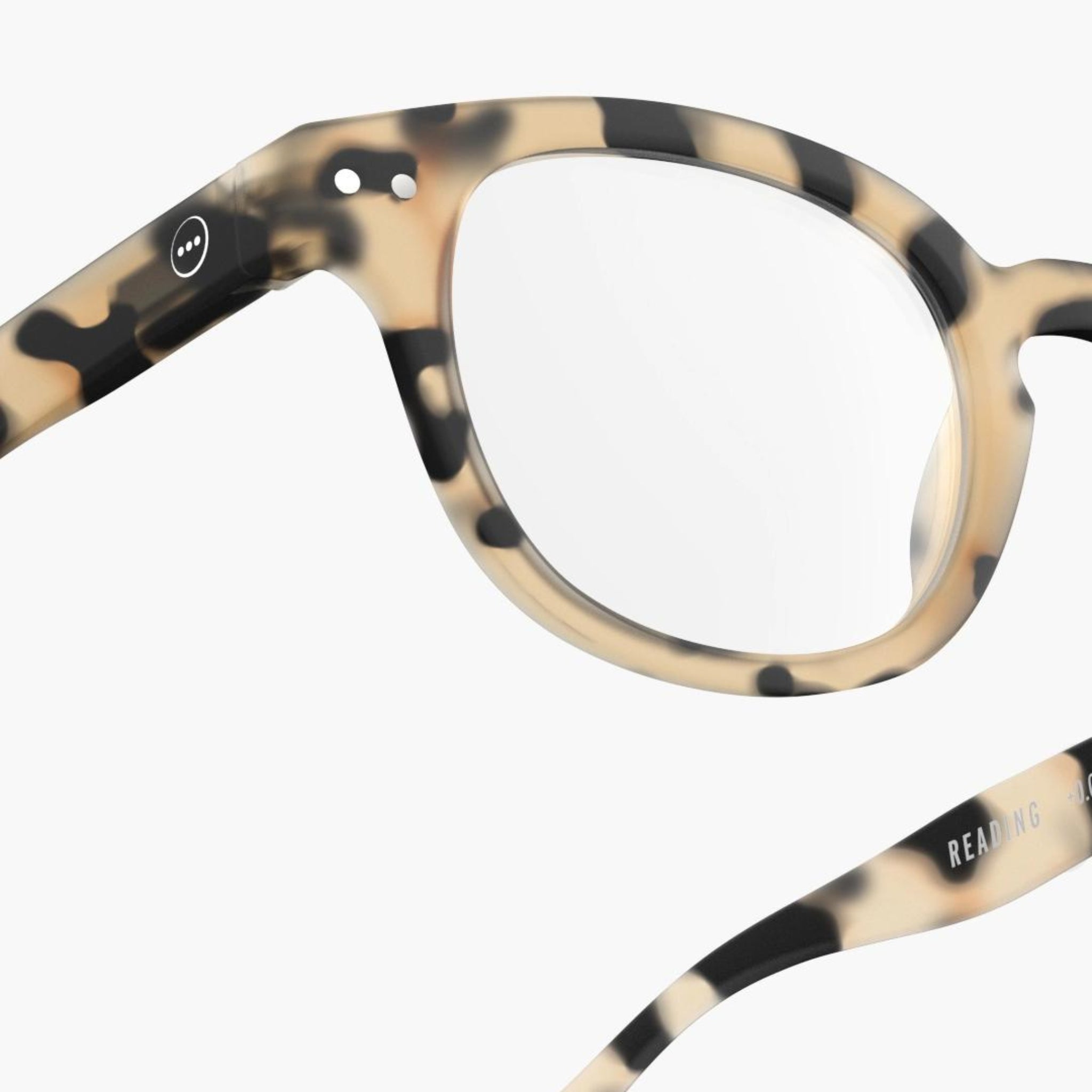 Close-up van Izipizi Leesbril #C Light Tortoise van Izipizi, een ronde leesbril in beige en zwart schildpadmotief - ideaal om presbyopie met stijl aan te pakken. "READING" is aan de binnenkant van één arm gedrukt.