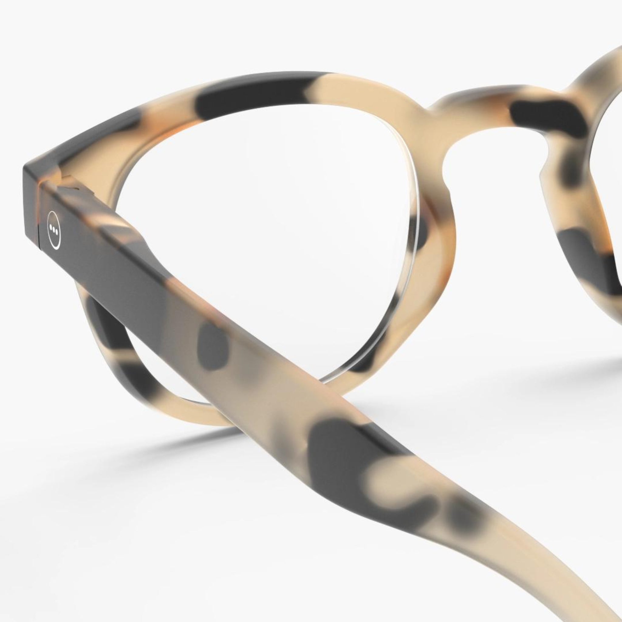Close-up van de Izipizi Leesbril #C Light Tortoise, een rond leesglas van Izipizi met een beige en zwart schildpadmontuur - perfect voor presbyopie - gezien vanaf de zijkant tegen een witte achtergrond.