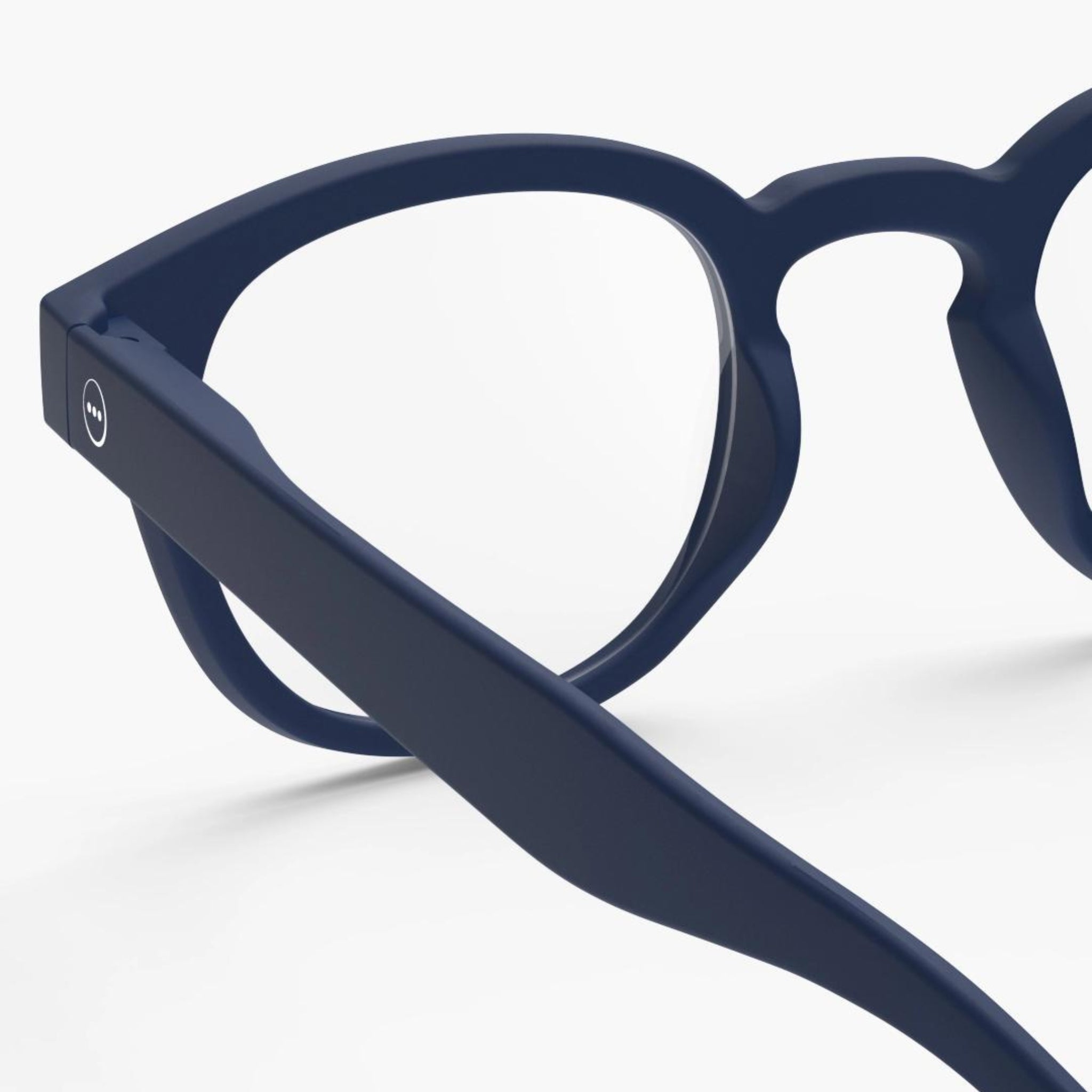 Close-up van de Izipizi Leesbril #C Navy van Izipizi, met een donkerblauw montuur en dikke matte slapen - een modern leesglas voor ouderdomsverziendheid - tegen een effen witte achtergrond.