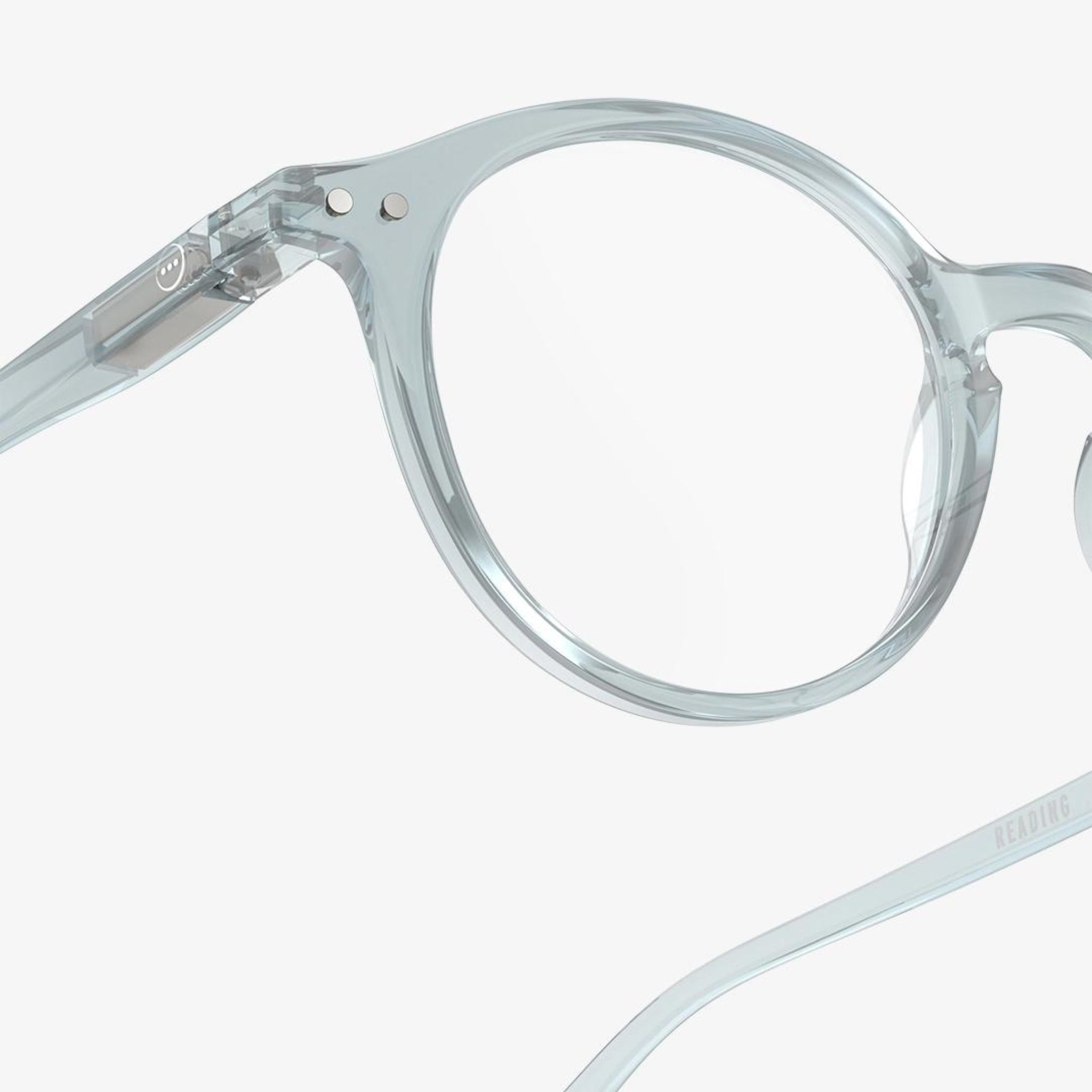 Close-up van transparant, rond Izipizi Leesbril #D Frozen Blue montuur tegen een witte achtergrond, met de linker lens en een deel van de veerarm van Izipizi, ontworpen voor comfortabele correctie van ouderdomsverziendheid.
