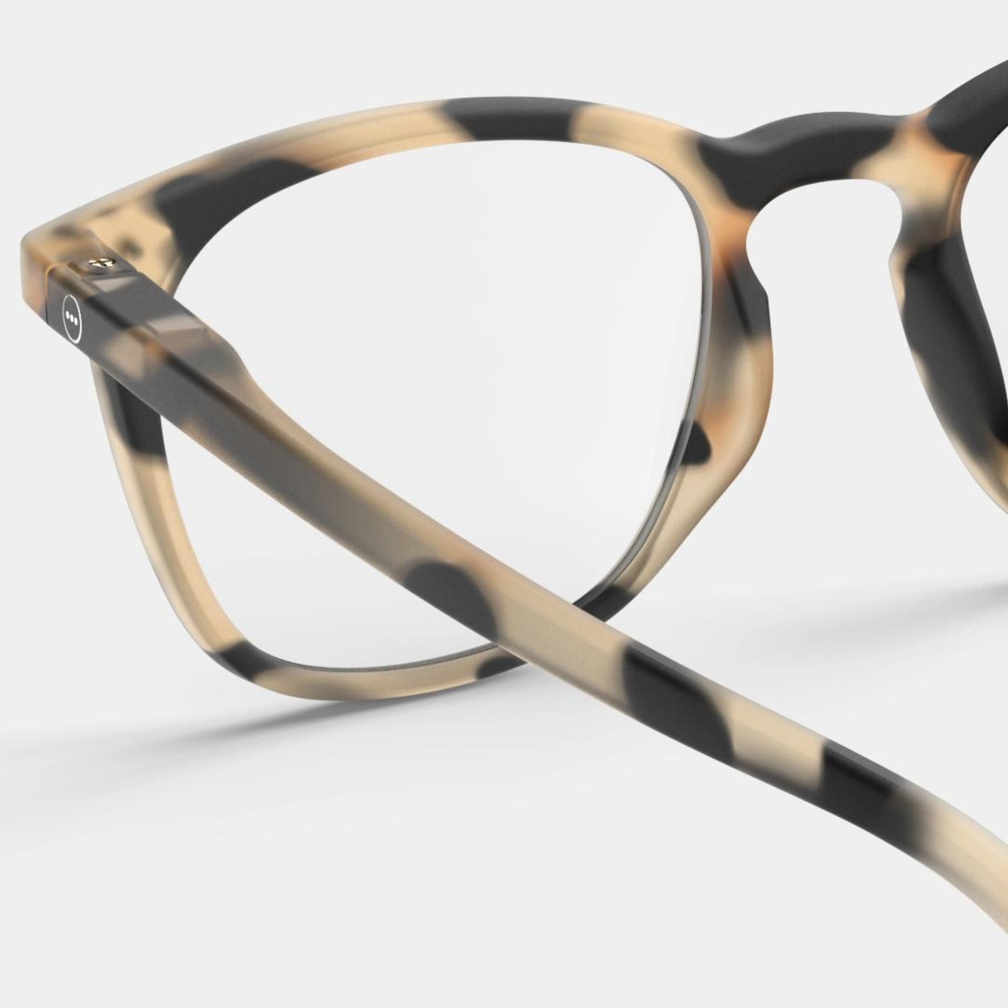Close-up van de Izipizi Leesbril #E Light Tortoise van Izipizi, een stijlvolle leesbril in schildpad beige, bruine en zwarte tinten voor mannen en vrouwen, afgebeeld tegen een effen lichte achtergrond.