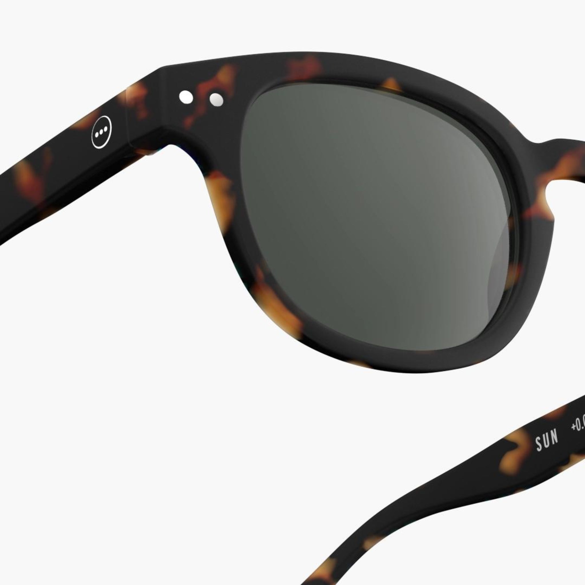 Close-up van de Izipizi Zonnebril Sterkte #C Tortoise: een unisex zonnebril met schildpadmotief van Izipizi, voorzien van donkere glazen, UV-bescherming en een klein cirkelvormig logo bij het scharnier op een witte achtergrond.