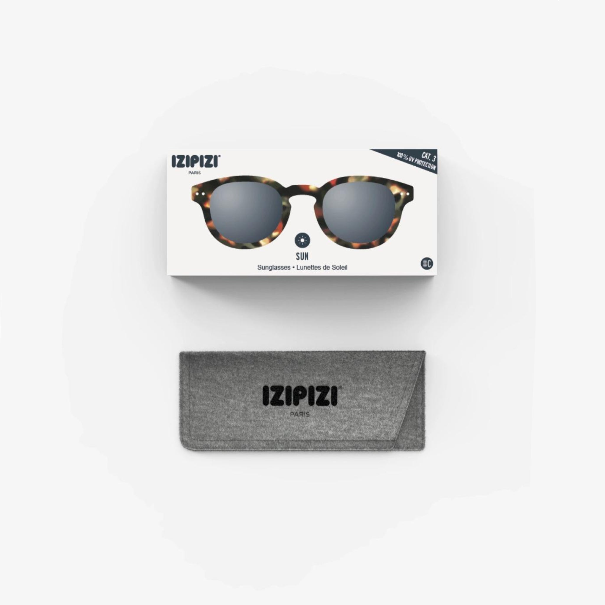 Een doosje van de Izipizi Zonnebril #C Tortoise van Izipizi zit boven een grijs etui met het merklogo - deze stijlvolle zonnebril van schildpad biedt perfecte UV-bescherming, allemaal gepresenteerd op een witte achtergrond.