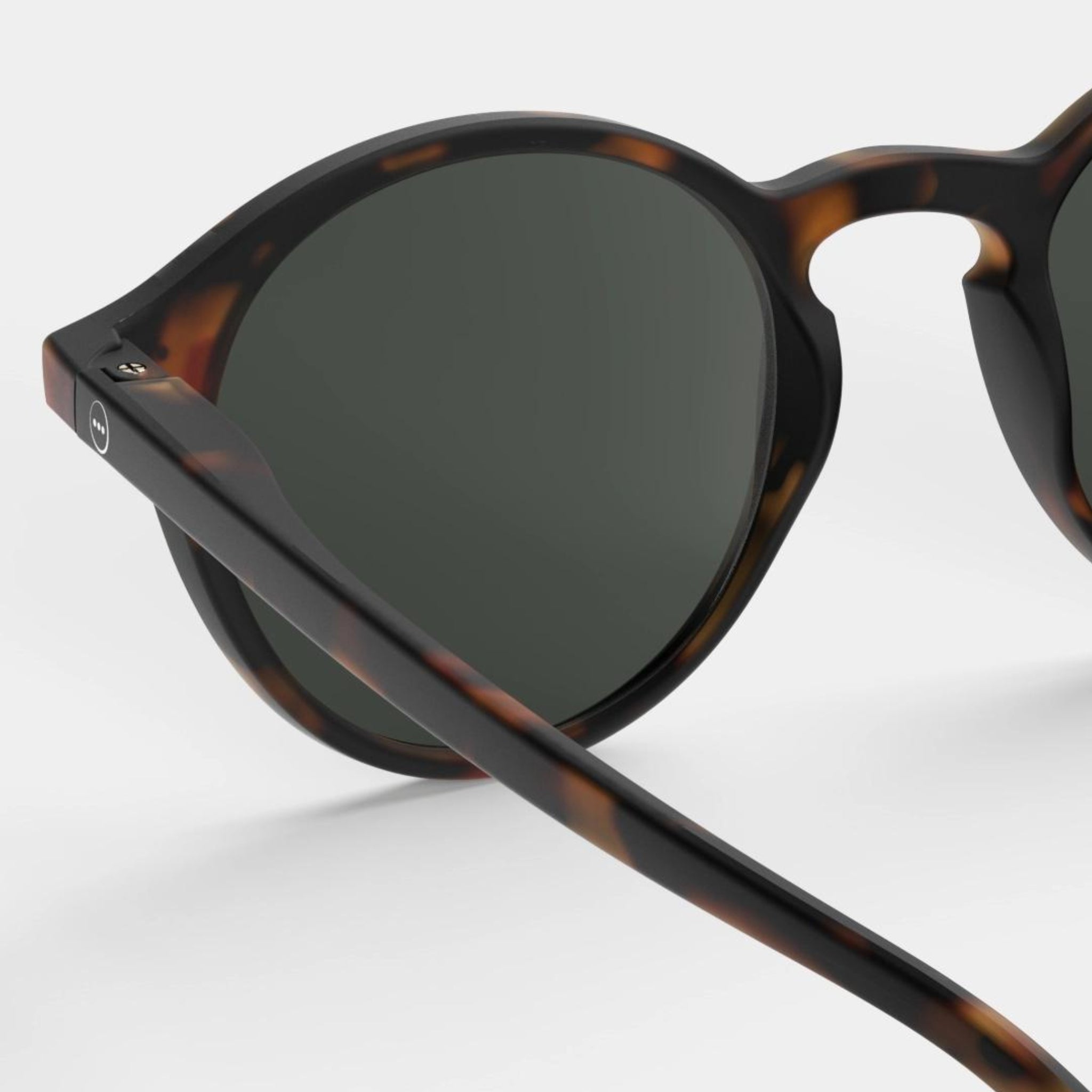 Close-up van de Izipizi Zonnebril #D Tortoise van Izipizi, met een stijlvol schildpadmontuur en donker getinte glazen voor UV-bescherming, afgebeeld tegen een lichte achtergrond.