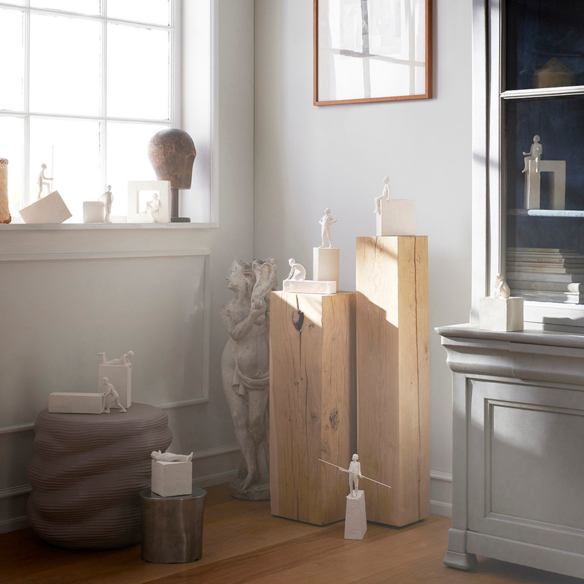 Lichte kamer met zonlicht, kleine witte menselijke beeldjes op houten blokken, minimalistisch decor, een sculptuur van paard en ruiter en de elegante Kähler Astro Sterrenbeeld Sculptuur Ram van Kähler die overal staat.