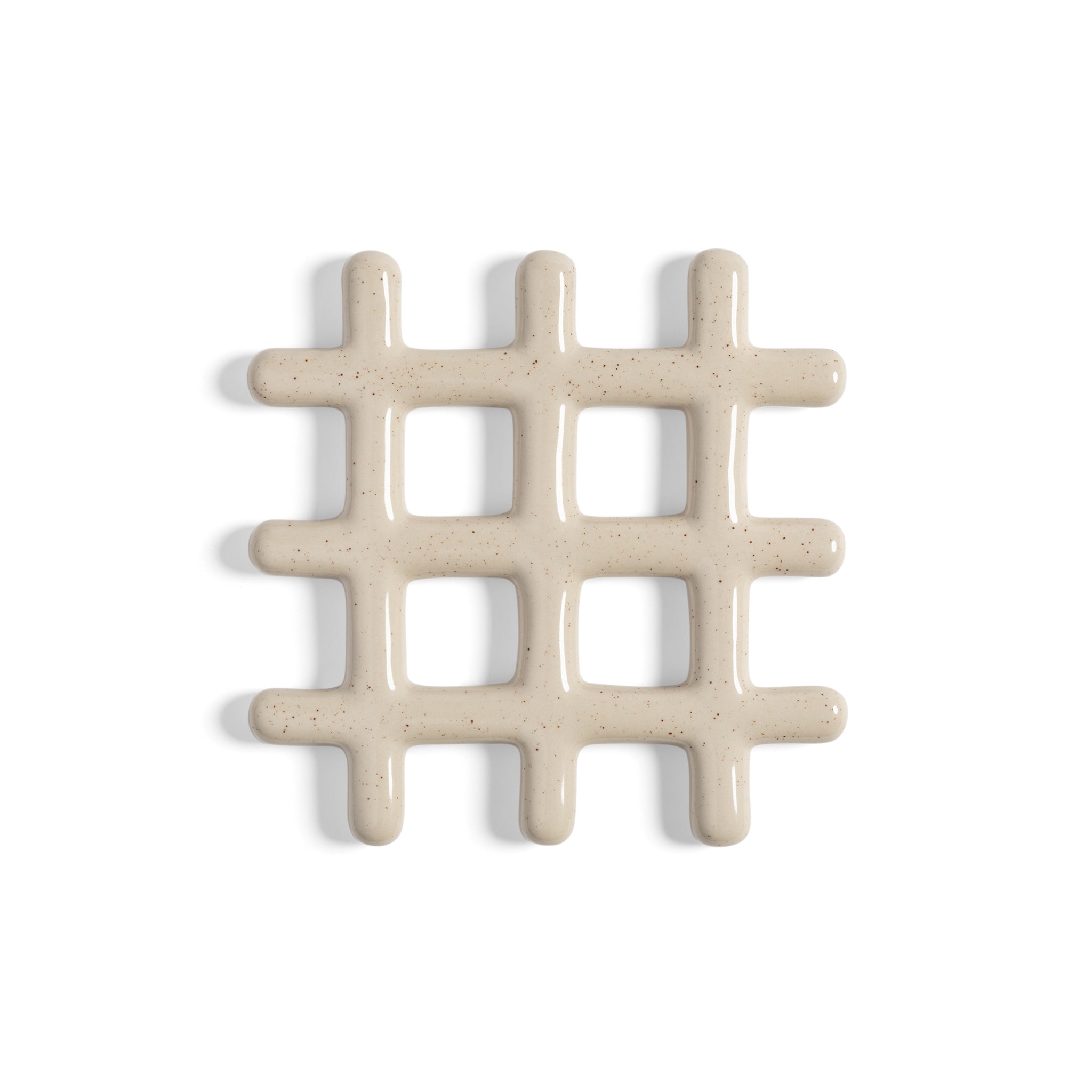 De &Klevering Grid Onderzetter Spikkel D19 is een beige, glanzend keramisch onderzetter met afgeronde hoeken en negen open vierkanten, die zachte schaduwen werpen op een witte keukenachtergrond.
