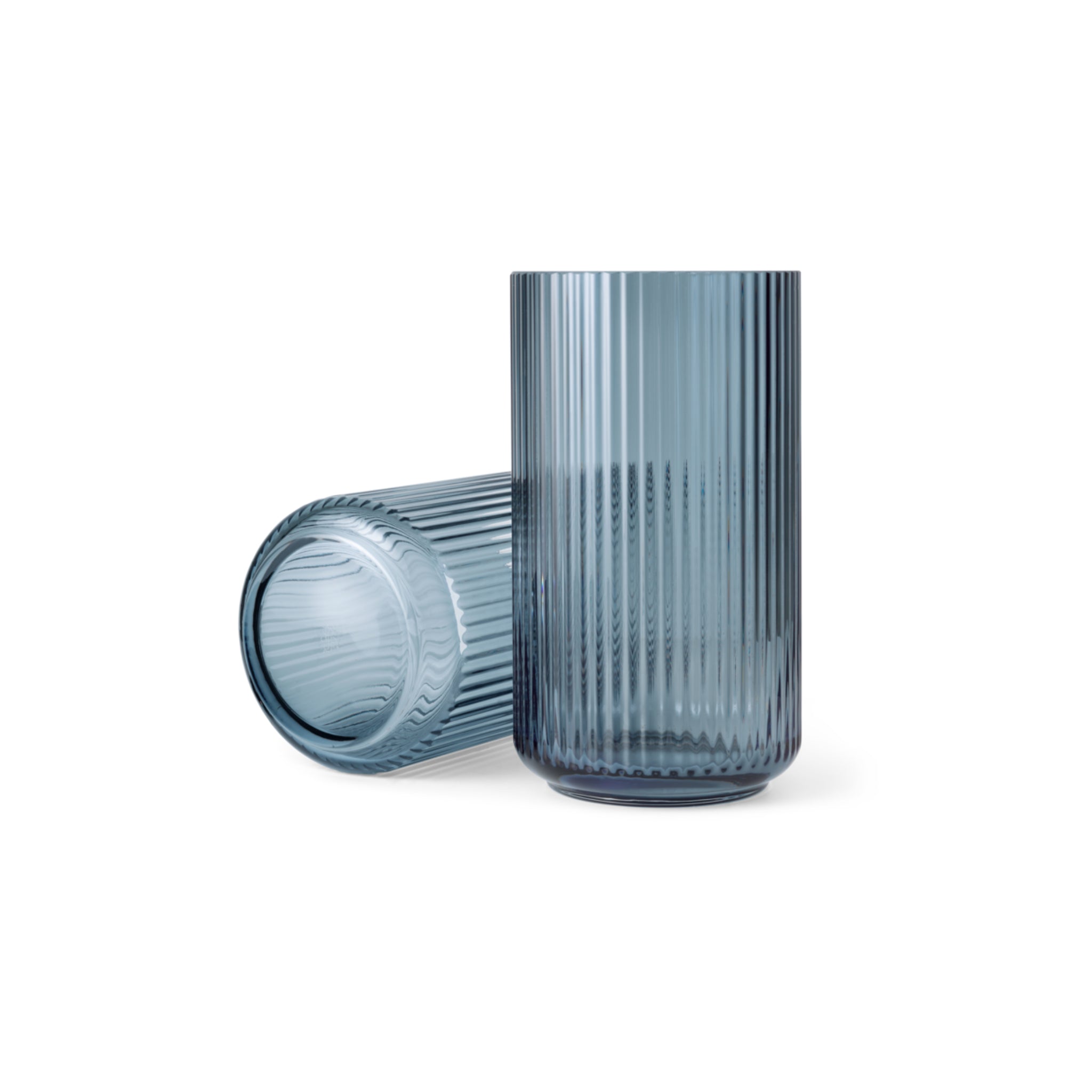 Twee Lyngby Porcelaen Vaas Blauw H31 glazen vazen van Lyngby Porcelaen, met een verticale geribbelde textuur en gemaakt van mondgeblazen glas, worden getoond - een rechtopstaand en een liggend - op een effen witte achtergrond.