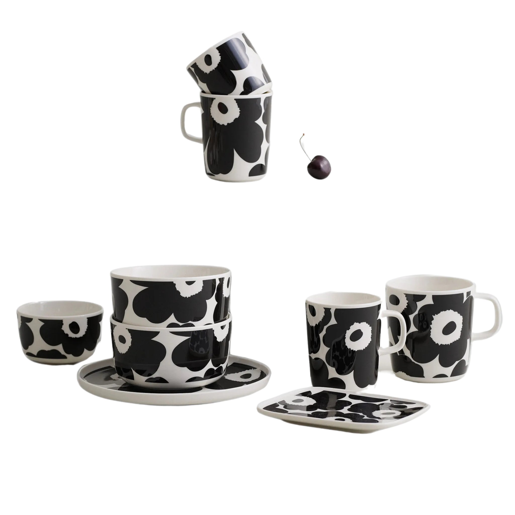 Een set Marimekko Oiva Unikko Laag Bord Zwart D20 zwart-wit steengoed met Unikko bloemenprint, bestaande uit borden, kommen en drie gestapelde mokken, wordt getoond. Een enkele kers en de mokken worden apart bovenaan getoond. Merk: Marimekko.