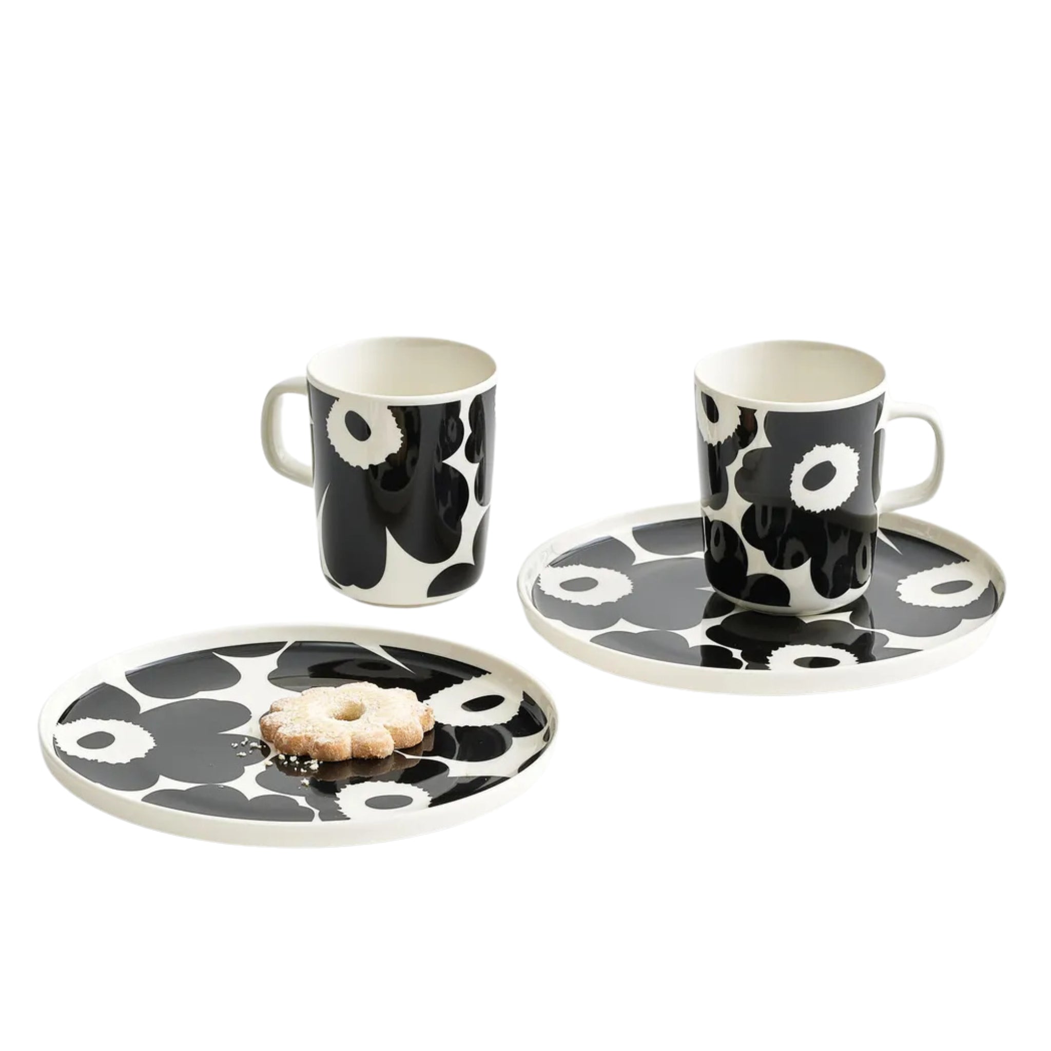 Twee keramische mokken en twee Marimekko Oiva Unikko Laag Bord Zwart D20 borden met een zwart-witte bloemenprint staan op een wit oppervlak, met drie koekjes op een van de borden.