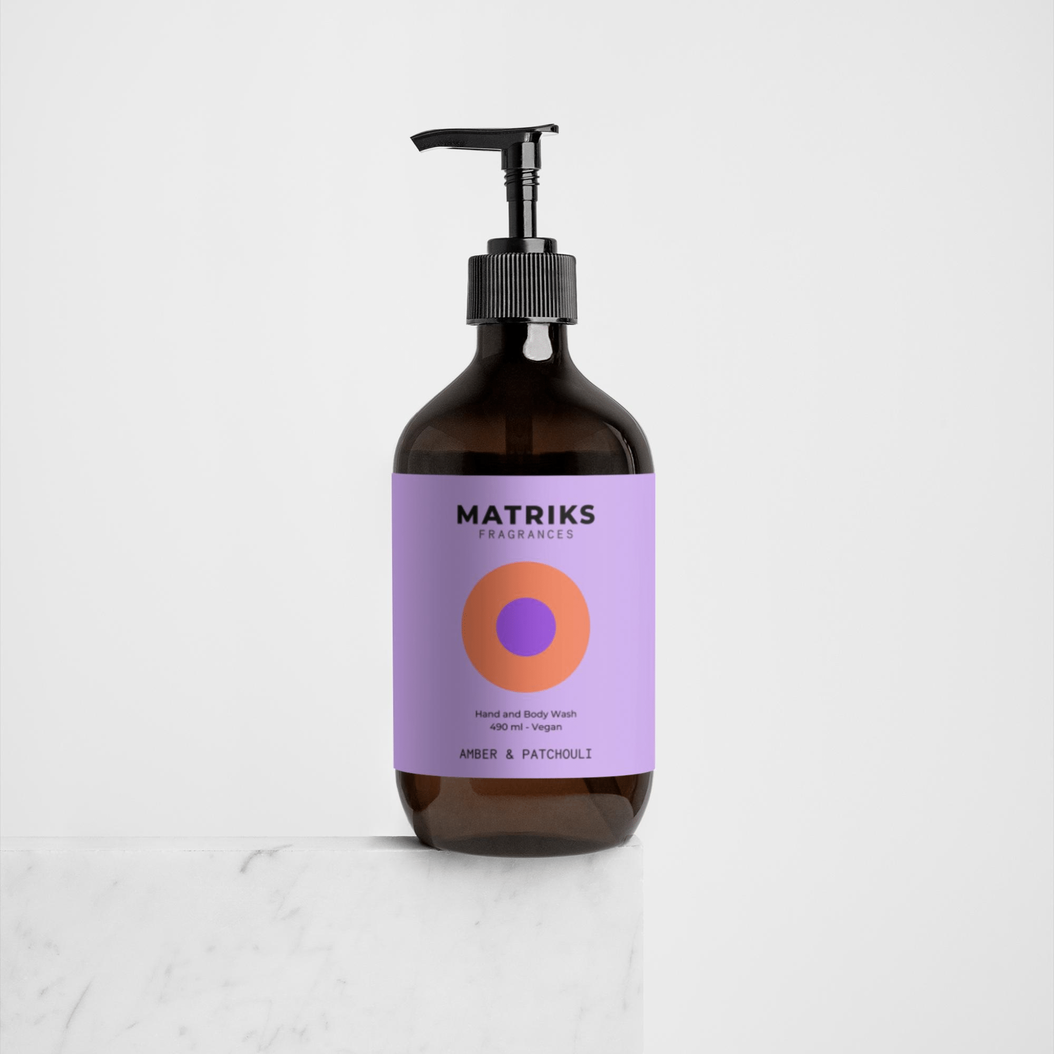 De bruine pompflacon van Matriks Fragrances Hand & Body Wash Amber & Patchouli 490 ml staat op een wit oppervlak. Het lichtpaarse etiket met cirkelvormig design benadrukt deze veganistische, stijlvolle en geurige body wash.