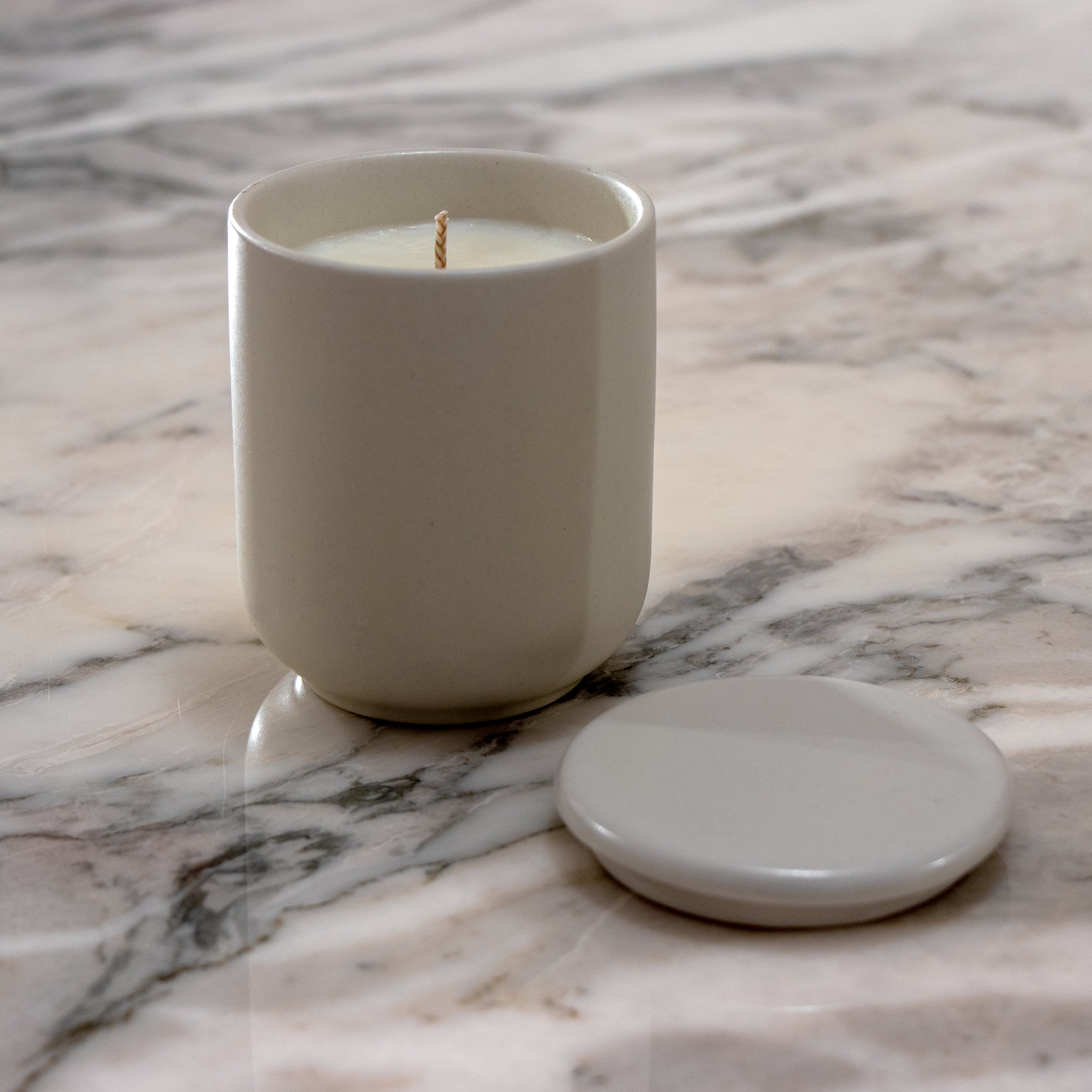 De Matriks Fragrances Geurkaars Keramiek Sweet & Smokey 270 g staat in een eenvoudig, rond keramieken potje op een marmeren oppervlak, met het bijpassende deksel ernaast.