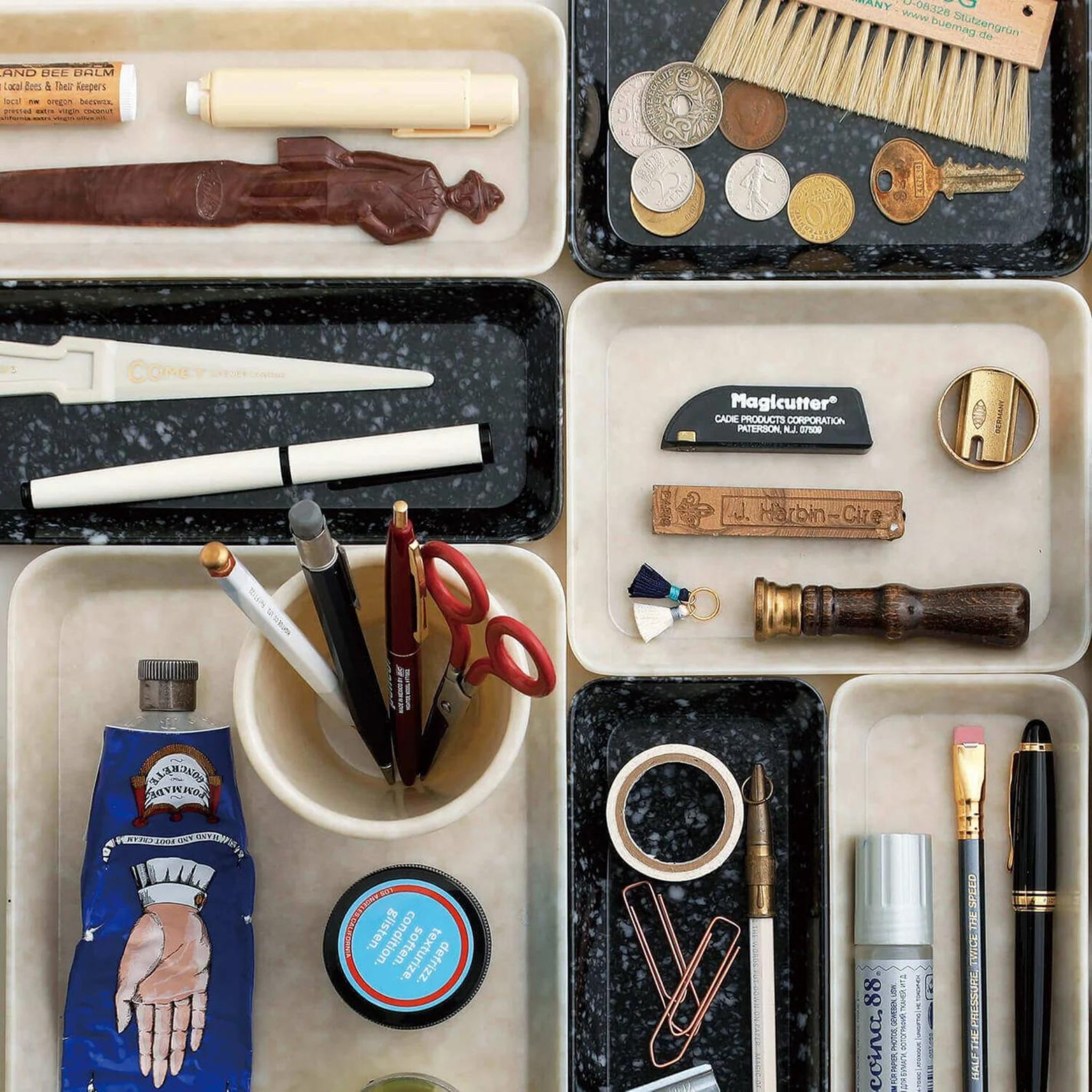 Een netjes georganiseerde lade met een bureau-organizer biedt plaats aan munten, penselen en meer, zelfs een Melamine Marbled Beker Ivoor van Melamine Marbled op een donker gespikkeld oppervlak.