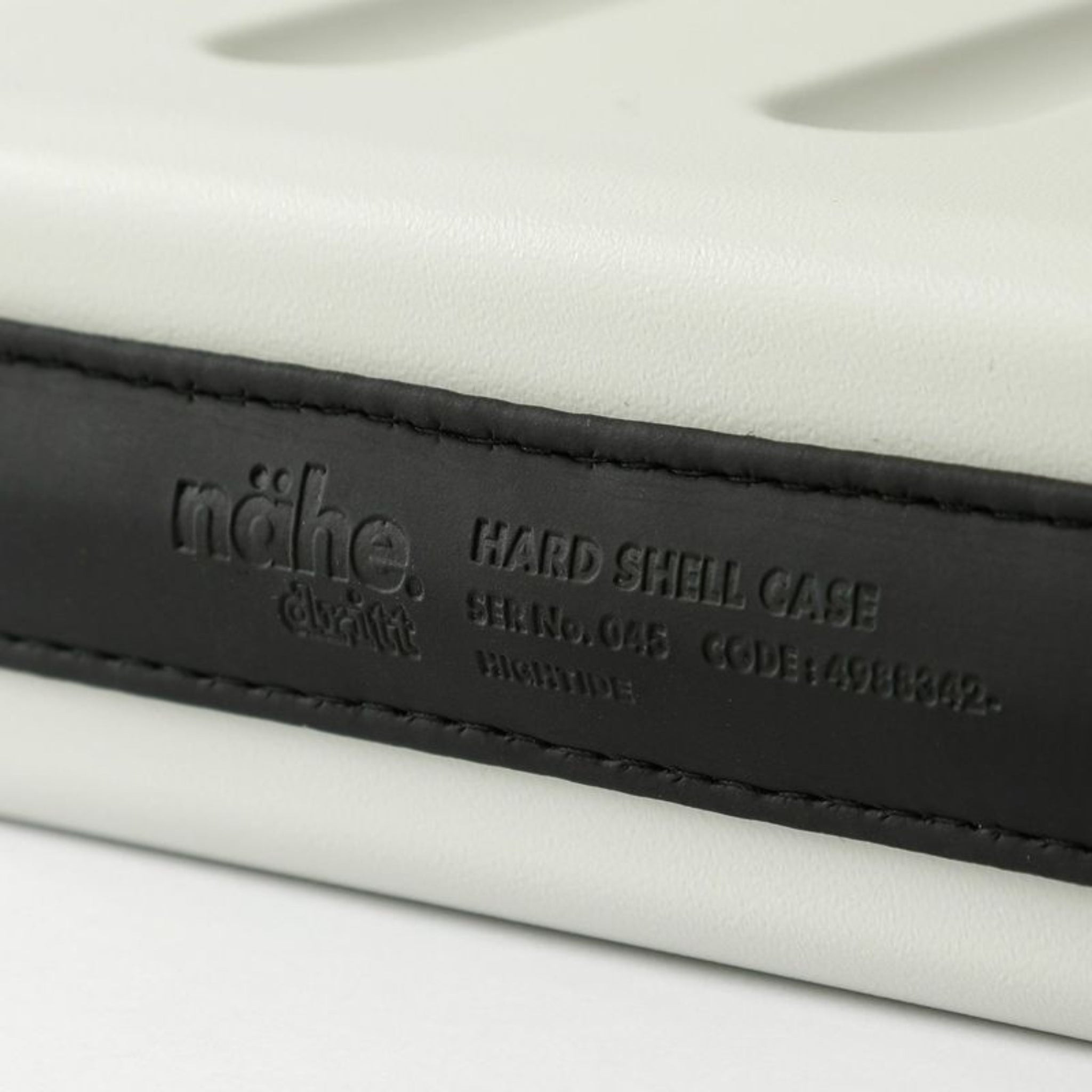 Close-up van de Nähe Hard Shell Organizer Ivoor S, een witte polycarbonaat koffer met zwarte band met in reliëf "nähe" en "HARD SHELL CASE S/N: 045 CODE: 4988342," plus decoratieve stiksels - ideaal voor gadgets.