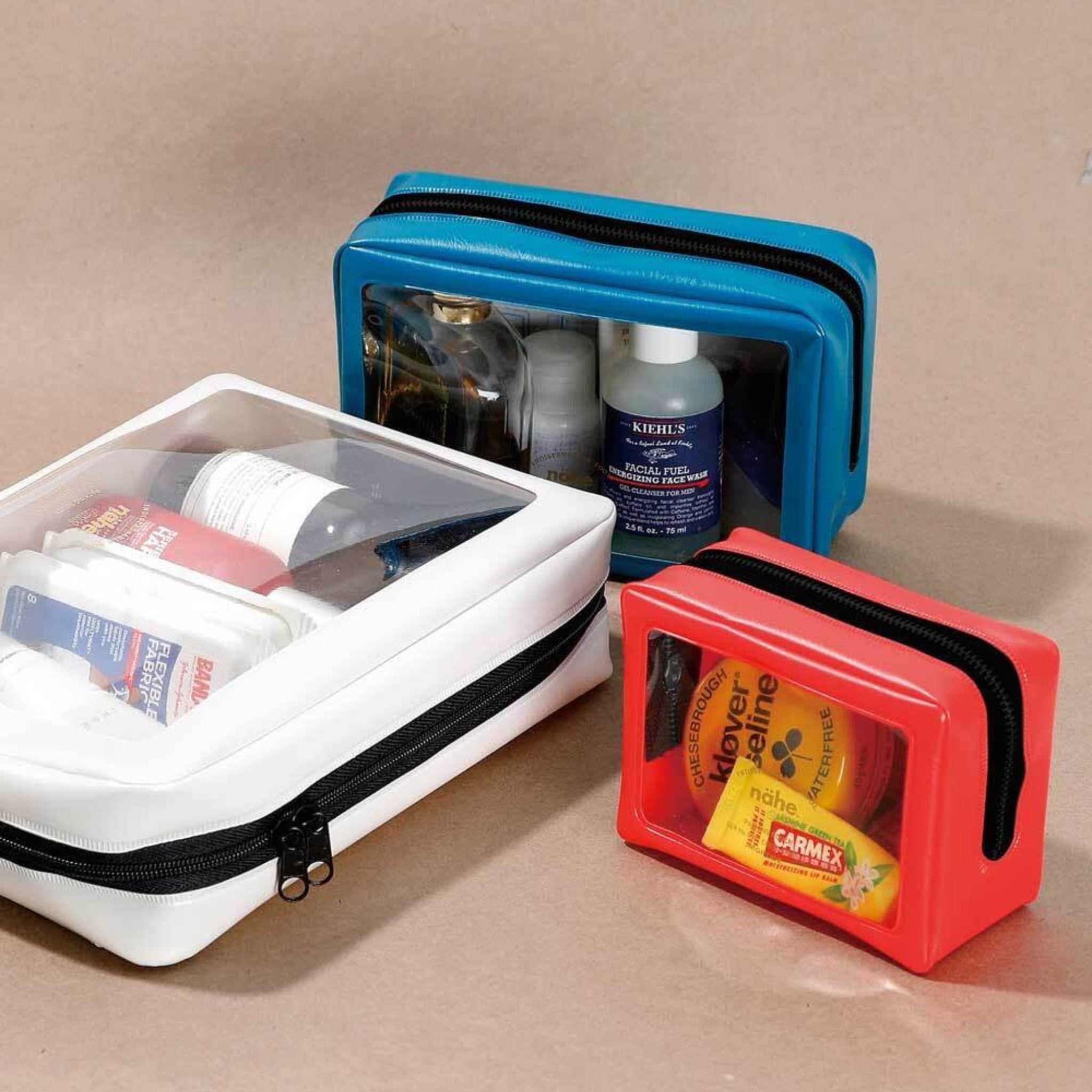 Een zwarte Nähe Reiszakje Zwart L toilettas van Nähe met een doorzichtig venster, met daarin verzorgingsproducten, uitgestald op een beige oppervlak.