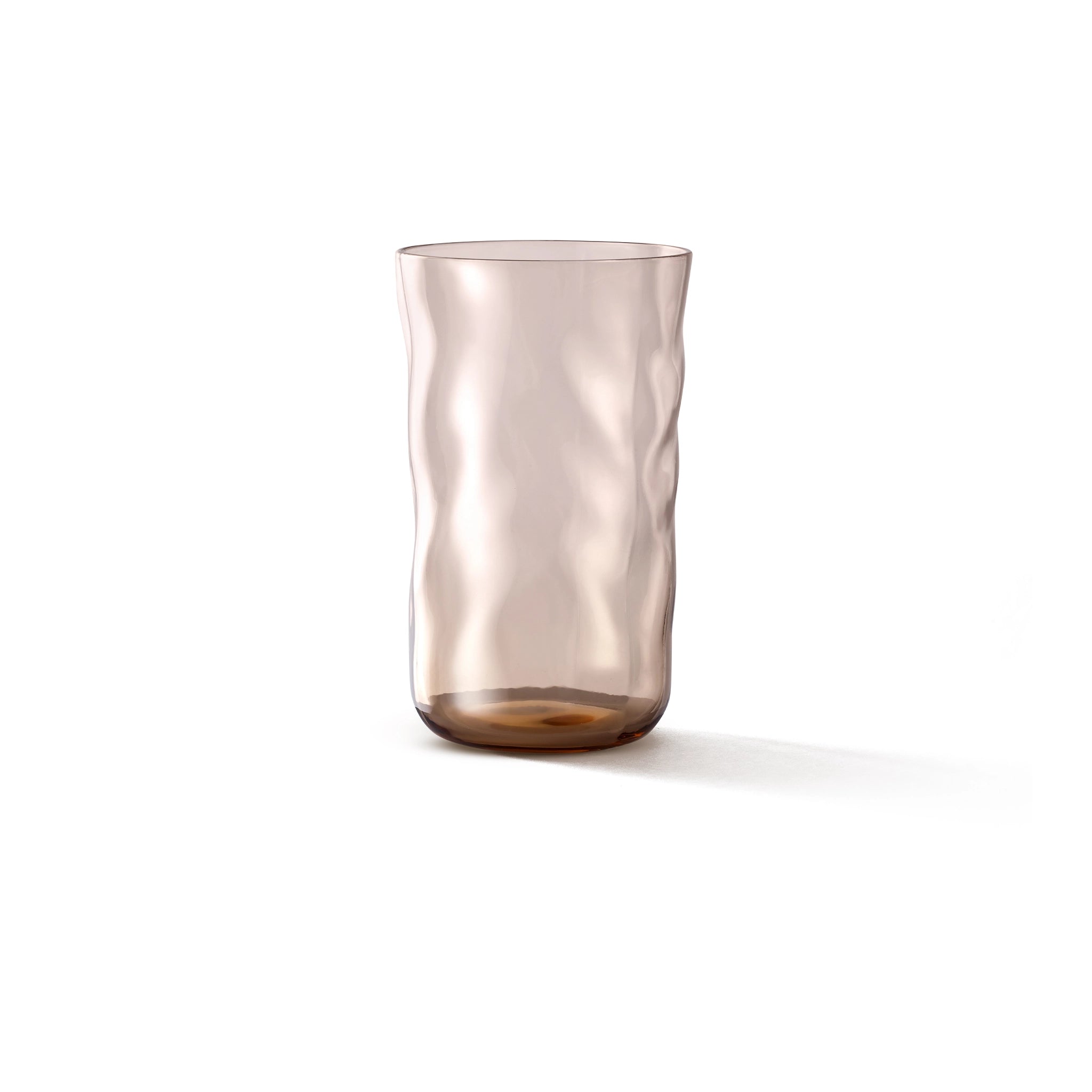 De Paveau Swirl Longdrink Glas Glow Beige 46 cl van Paveau heeft een doorschijnende, lichtbruine tint met een golvend, gestructureerd oppervlak. Deze cilindrische glazen beker van borosilicaatglas is afgebeeld op een witte achtergrond met een zachte schaduw aan de rechterkant.