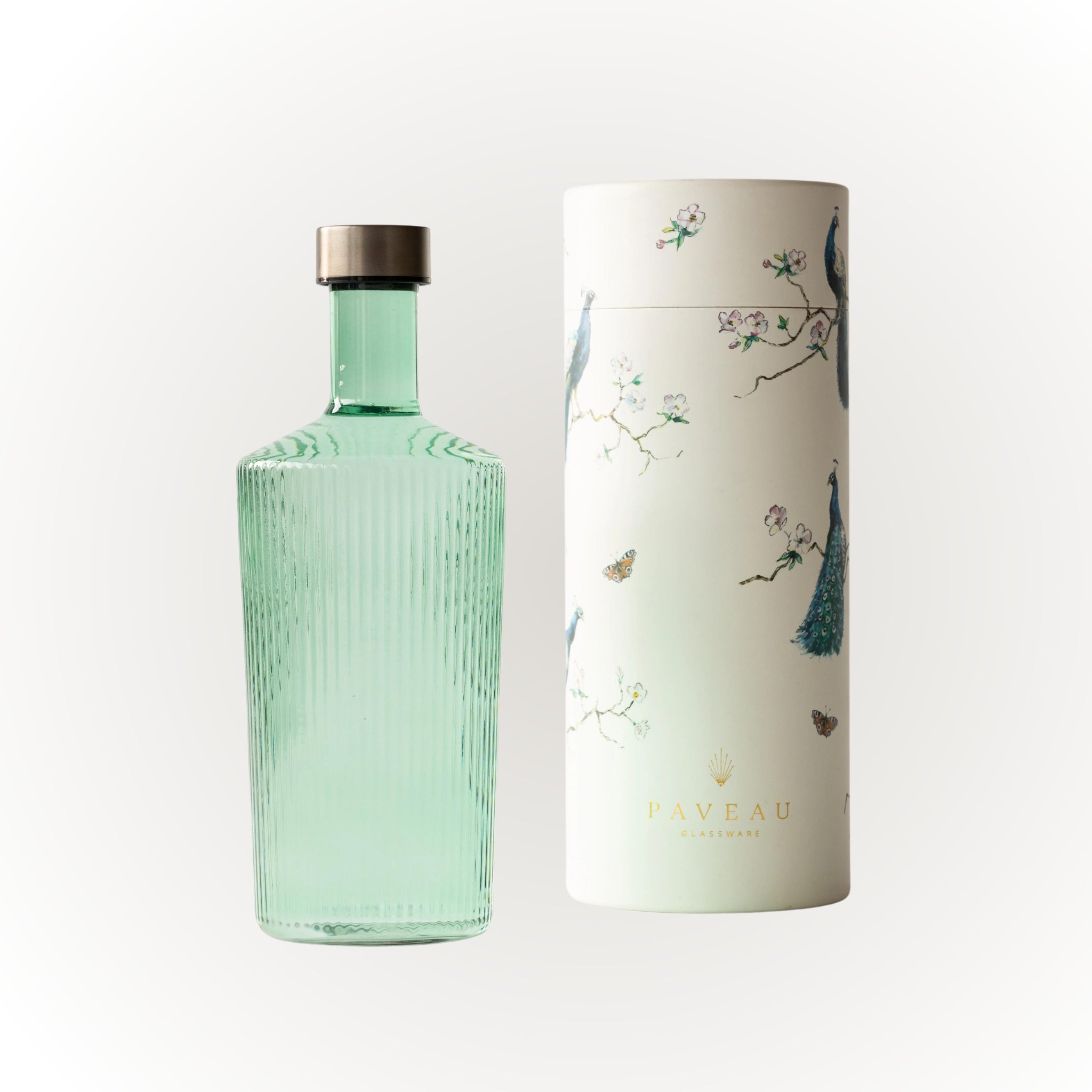 De Paveau Waterfles Bondi Green 1,25 l - een geribbelde, lichtgroene fles met een metalen dop - staat naast een cilindervormige witte doos met illustraties van pauwen, bloemen en vlinders en de merknaam Paveau onderaan.