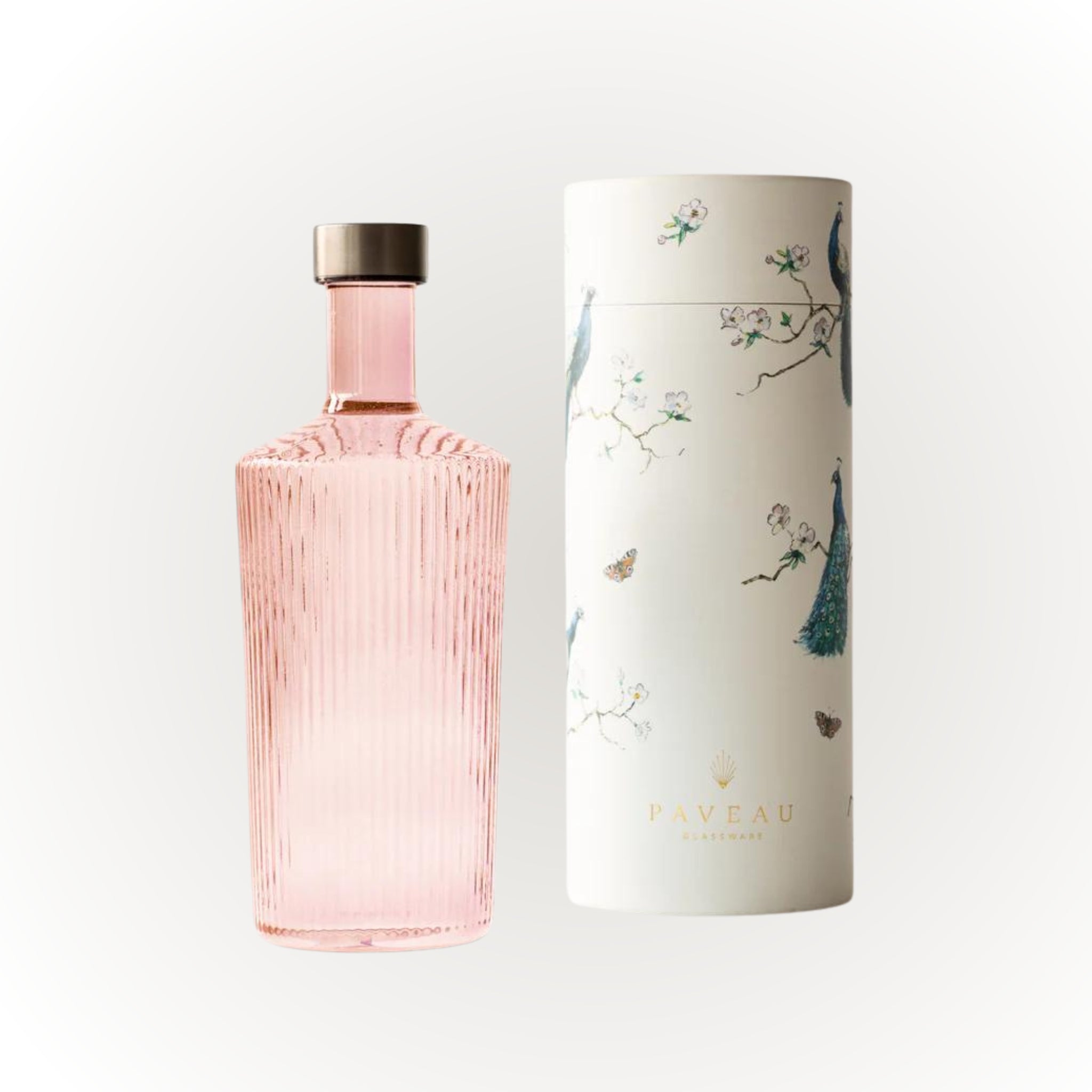 De Paveau Waterfles Pink 1,25 l met geribbeld design en metalen dop staat naast zijn witte cilindrische doos, versierd met illustraties van pauwen, takken en vlinders en de merknaam Paveau.