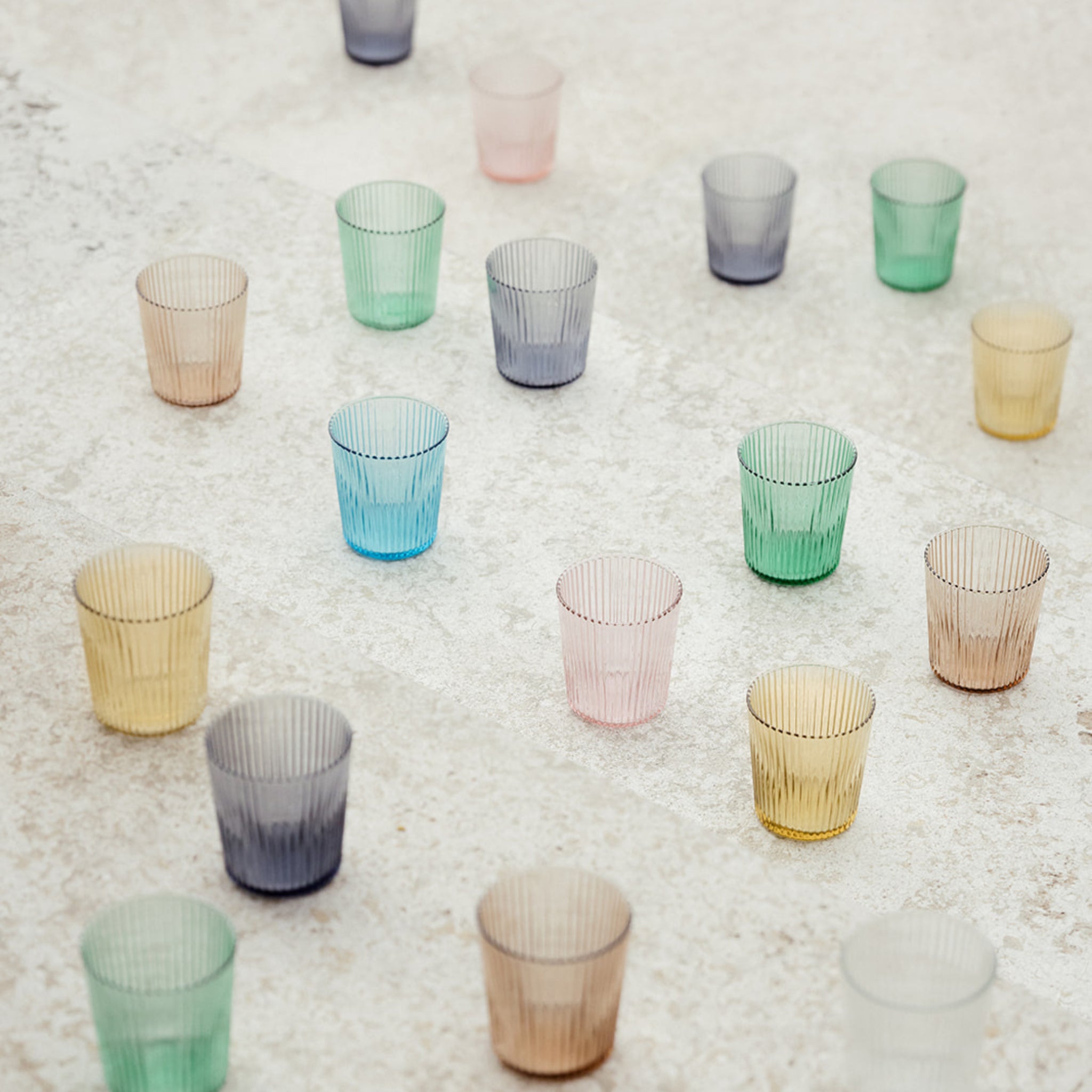 Een collectie Paveau Waterglas Twilight Blue van Paveau, met een geribbeld ontwerp, is kunstig gerangschikt op een licht gestructureerd oppervlak. Deze duurzame glazen hebben opvallende blauwe tinten.