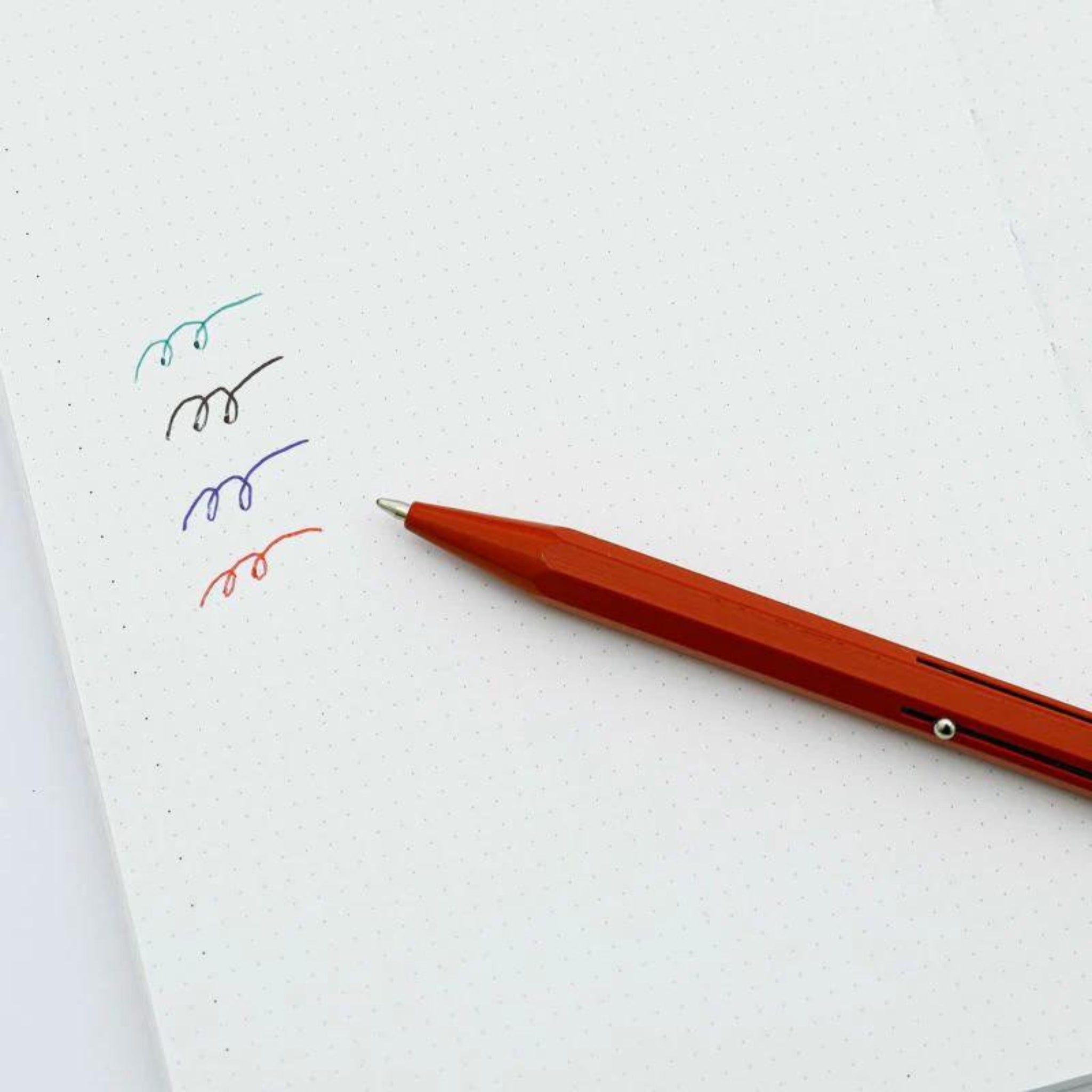 Een Penco 4 Kleuren Balpen Munt van Penco zit op een gestippelde notitieboekpagina en toont vijf gekleurde tilde - groen, zwart, paars, blauw en rood - om de verschillende inktkleuren te laten zien die deze vintage-geïnspireerde pen biedt.