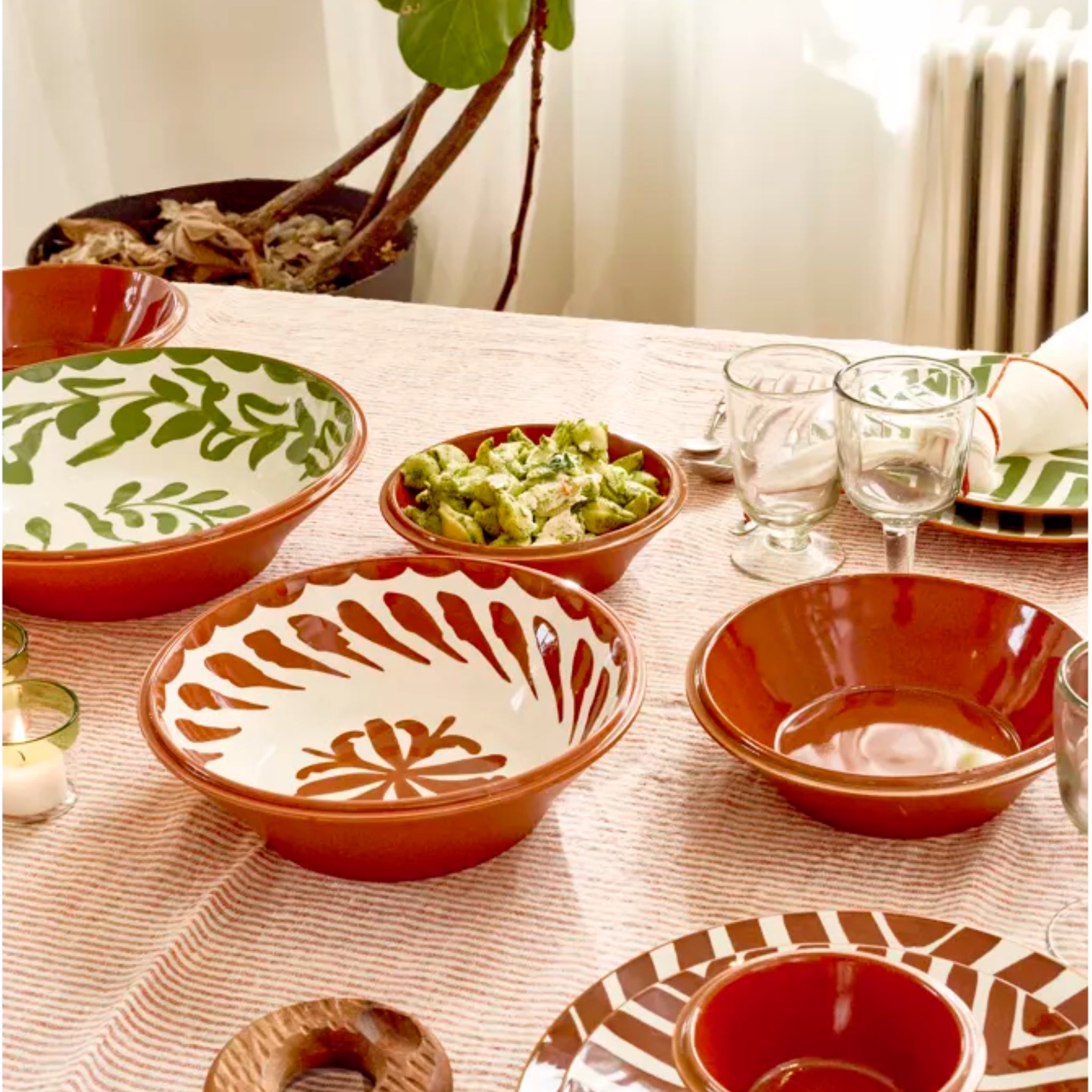 Een gedekte tafel met keramische schalen van Pomax Amuse Kom Bruin D21 - één gevuld met groene salade - omringd door drankjes, kaarsen en een potplant op de achtergrond.