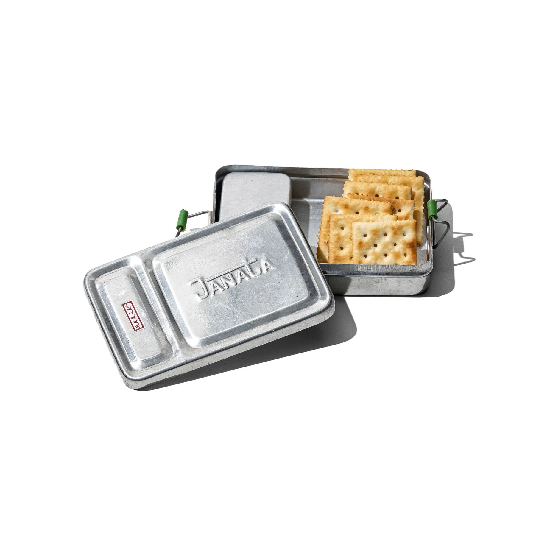 Een Puebco Aluminium Lunch Box met een gedeeltelijk geopend deksel onthult netjes gestapelde vierkante crackers binnenin, weergegeven op een witte achtergrond.