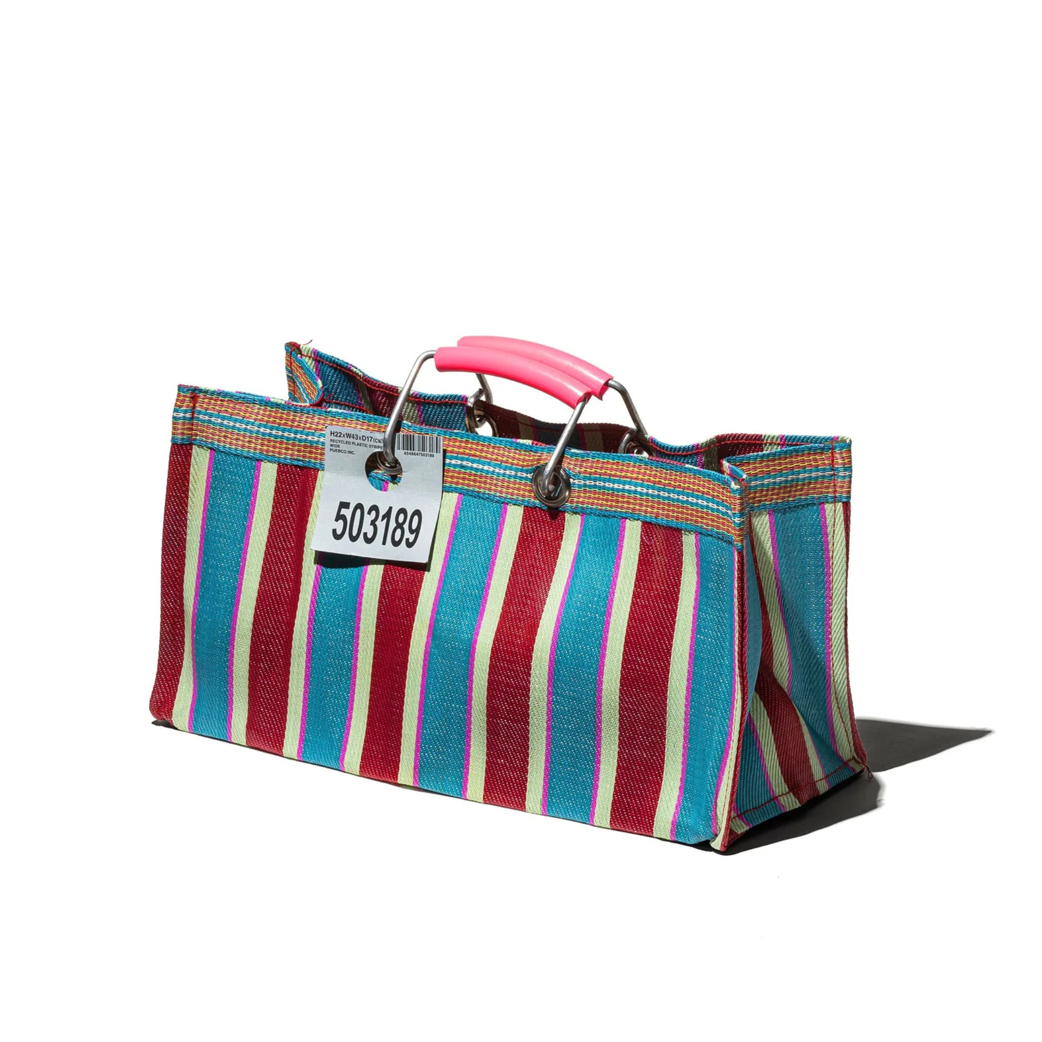 Een Puebco Gerecycleerde Tas Strepen Rood Blauw Breed van Puebco heeft opvallende blauwe, rode en roze strepen, een roze plastic handvat en een label met 503189, gefotografeerd op een witte achtergrond.