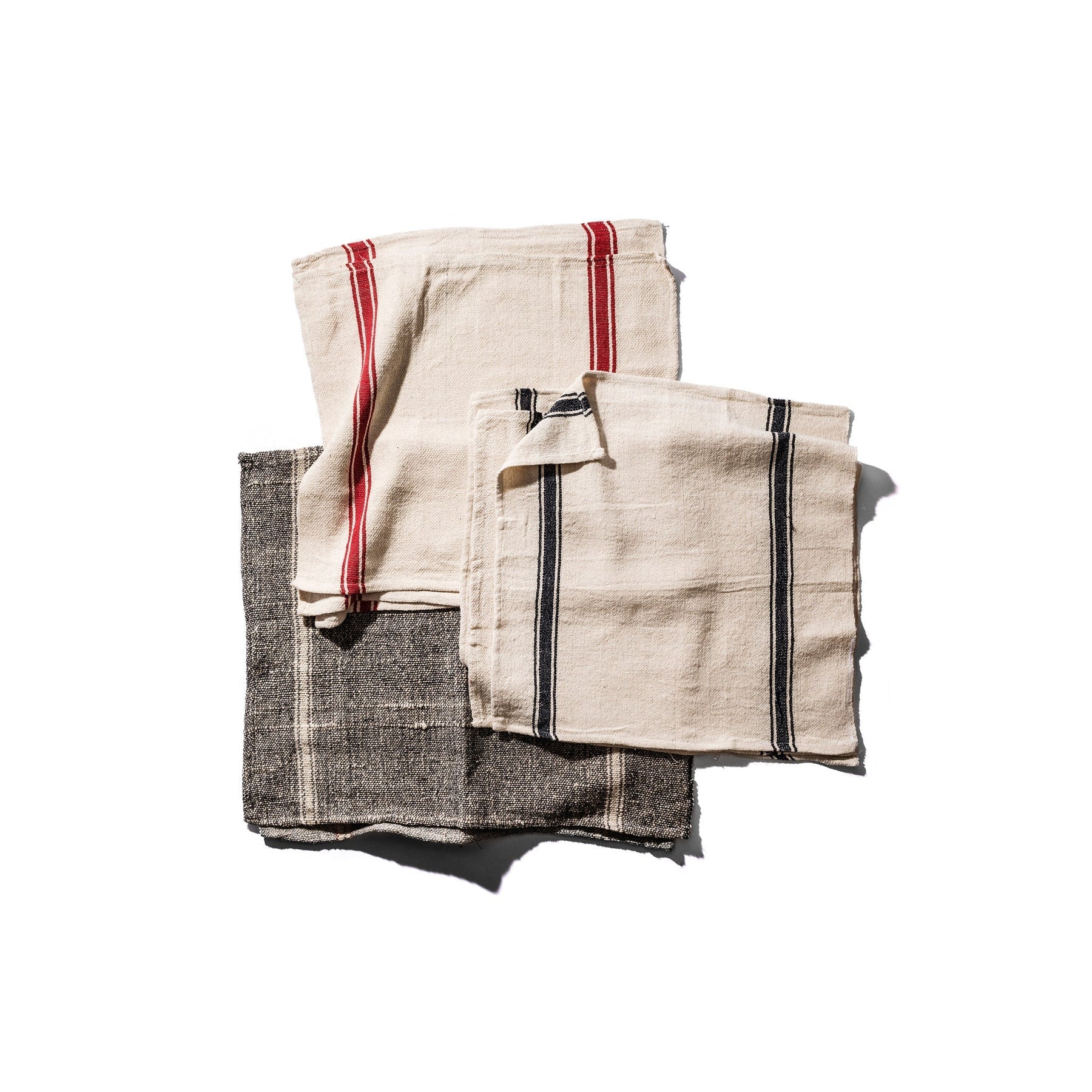 Drie gevouwen Puebco India Theedoek Zwart 60/60 servetten - beige met rode strepen, beige met zwarte strepen en donkergrijs (Theedoek Zwart) met witte strepen - zijn gemaakt van gerecycleerde stoffen in India en liggen op een witte achtergrond.