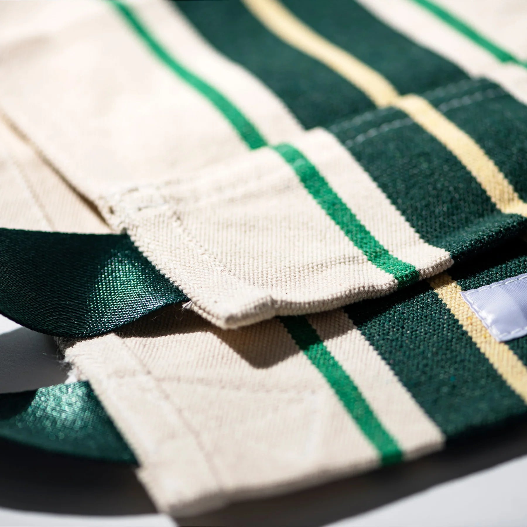 Close-up van de Puebco Magazinehouder Café Groen Strepen van Puebco, met de groene, gele en crèmekleurige gestreepte stof met een genaaide rand en groene band - ideaal voor het organiseren of hergebruiken van projecten. Textuur en stikseldetails zijn zichtbaar.