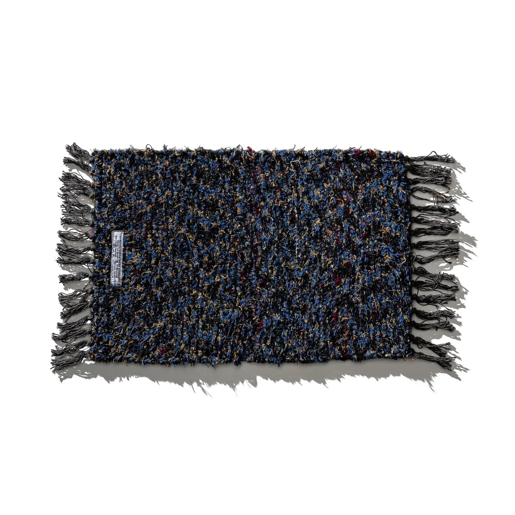 De Puebco Mat Gerecycleerd Textiel 63/41 is een rechthoekige mat van Puebco met veelkleurige blauwe, zwarte en gouden draden en gefranjerde randen, plat uitgelegd op een witte ondergrond.